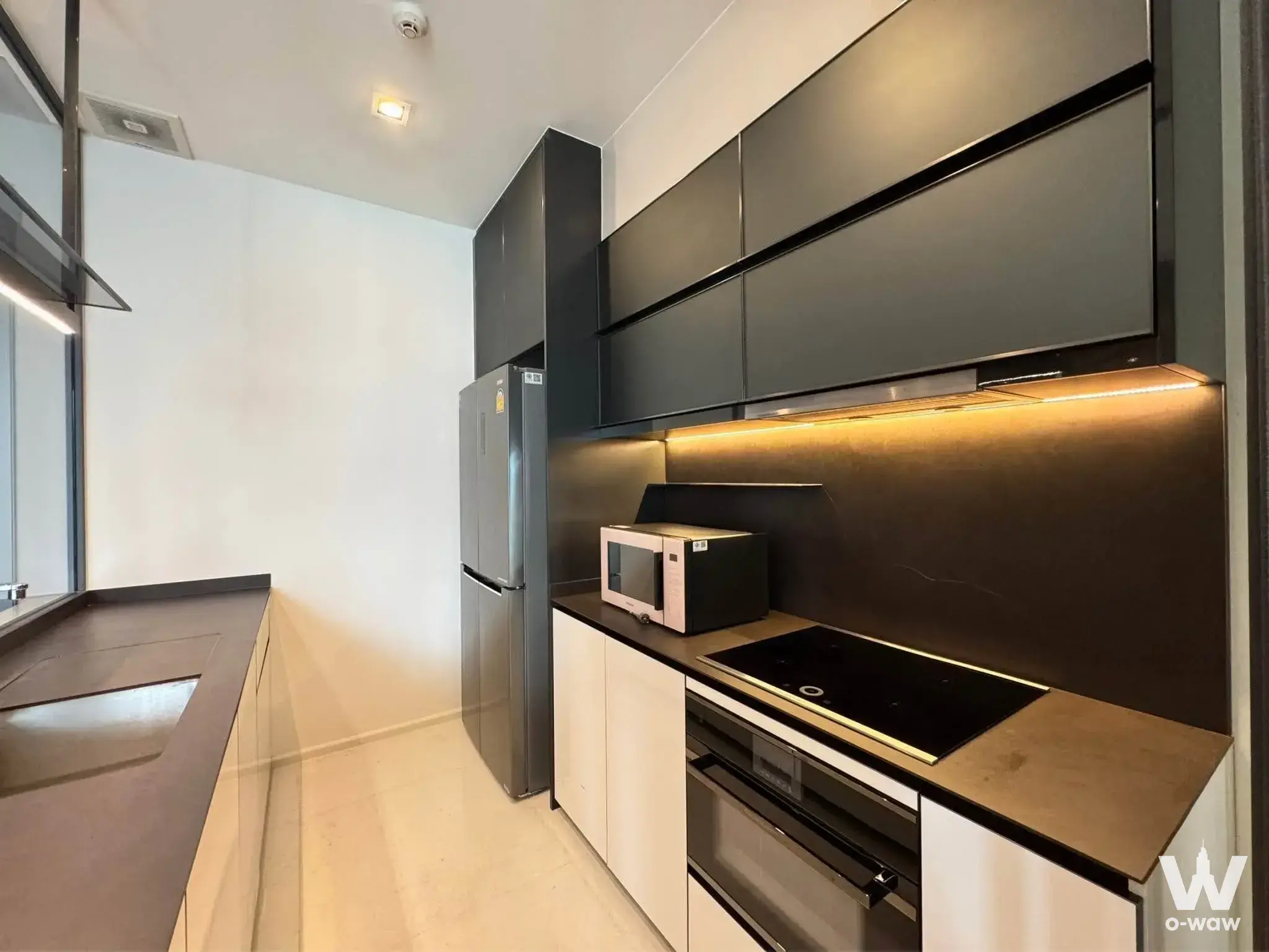 Modern galley kitchen with dark grey cabinets and stone counters in a 2-bed condo for rent in The Bangkok Thonglor