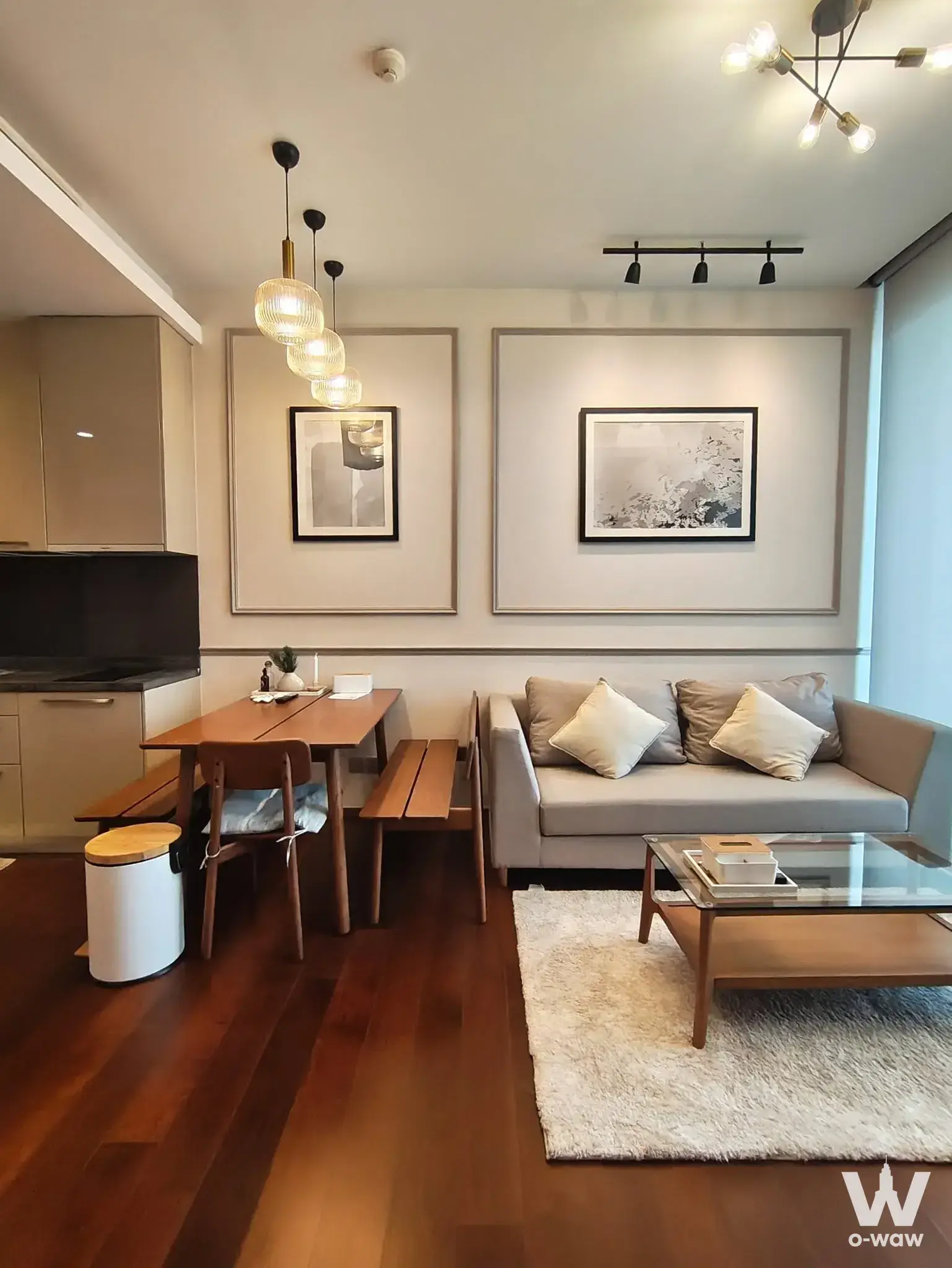 Open-plan living and dining area in a Quattro by Sansiri 1-bed condo featuring dark hardwood floors and a glass-top coffee