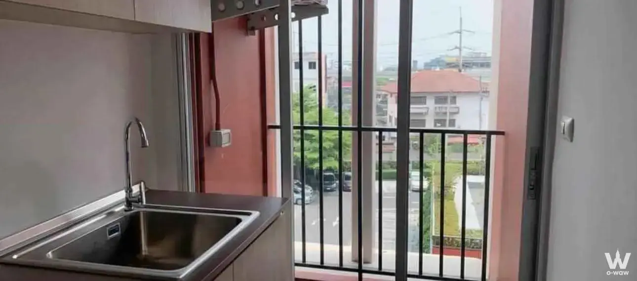 Compact kitchenette in Supalai Veranda Sukhumvit 117 with dark counter and glass door to balcony