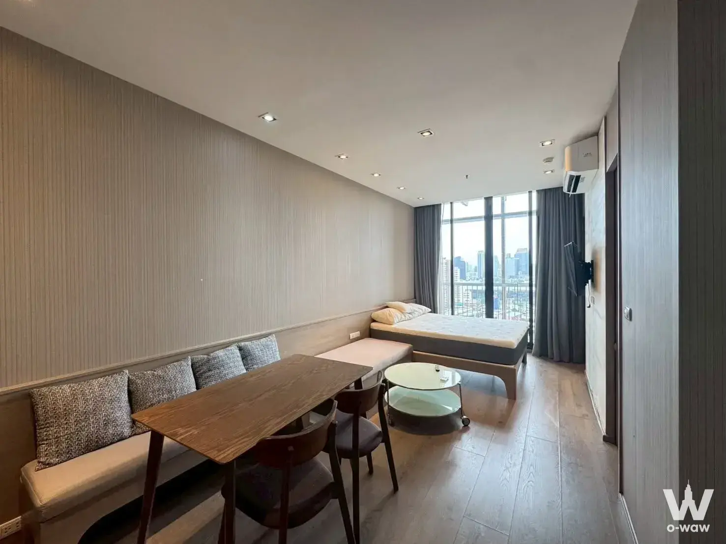 Open-plan Park24 studio with beige bench seating, dark wood dining table, and floor-to-ceiling windows