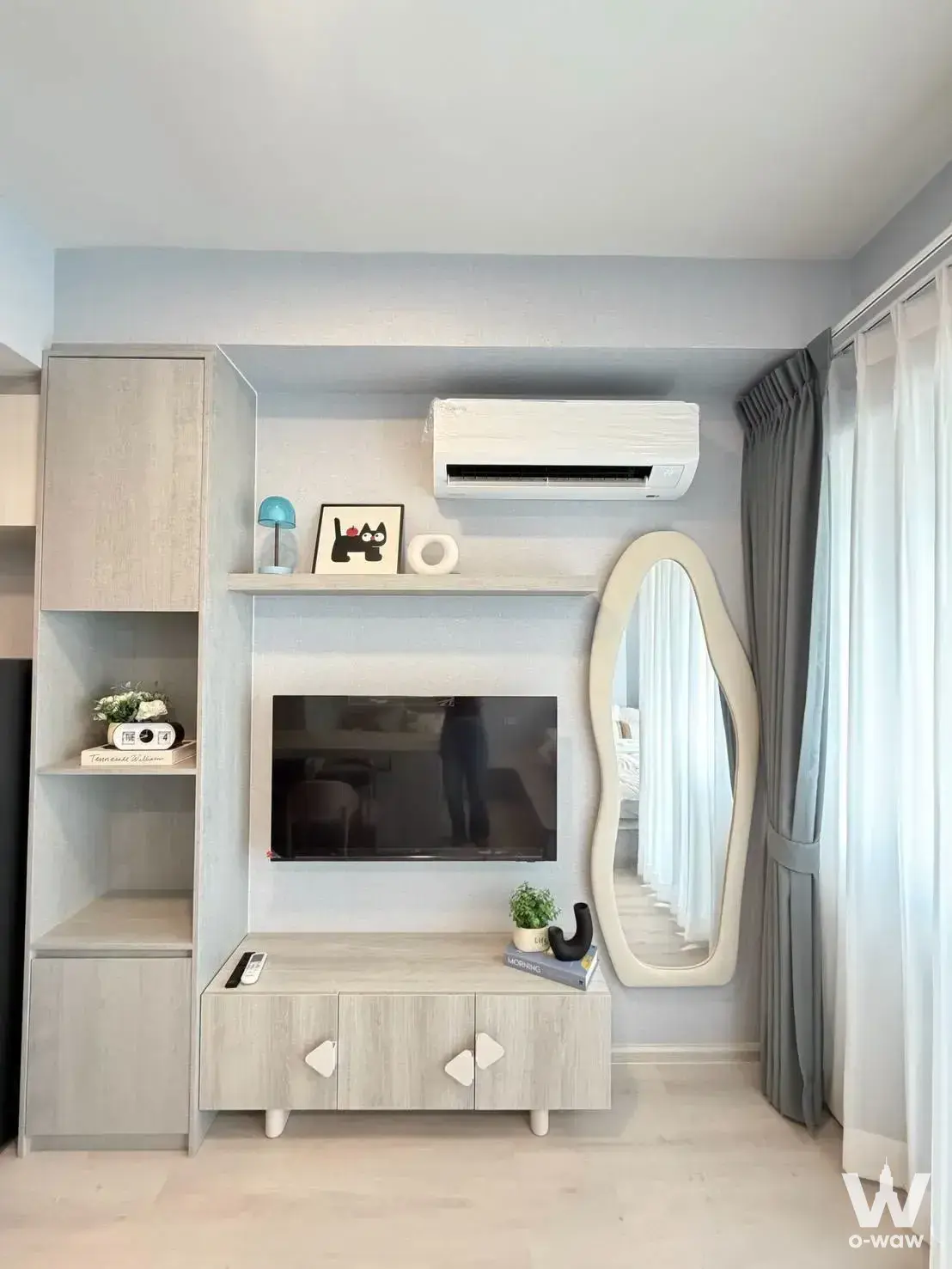 Living room in COBE Ratchada-Rama 9 1-bed condo with light-wood media wall, TV, and large organic floor mirror