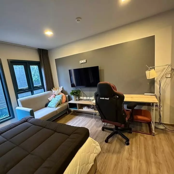Studio at THE BASE Sukhumvit 50 featuring a bed, beige sofa, and gaming chair near the window