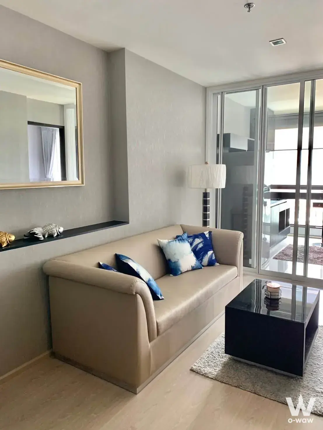 Modern living room in RHYTHM Sukhumvit 44 condo with beige sofa, blue accents, and sliding doors opening to a balcony