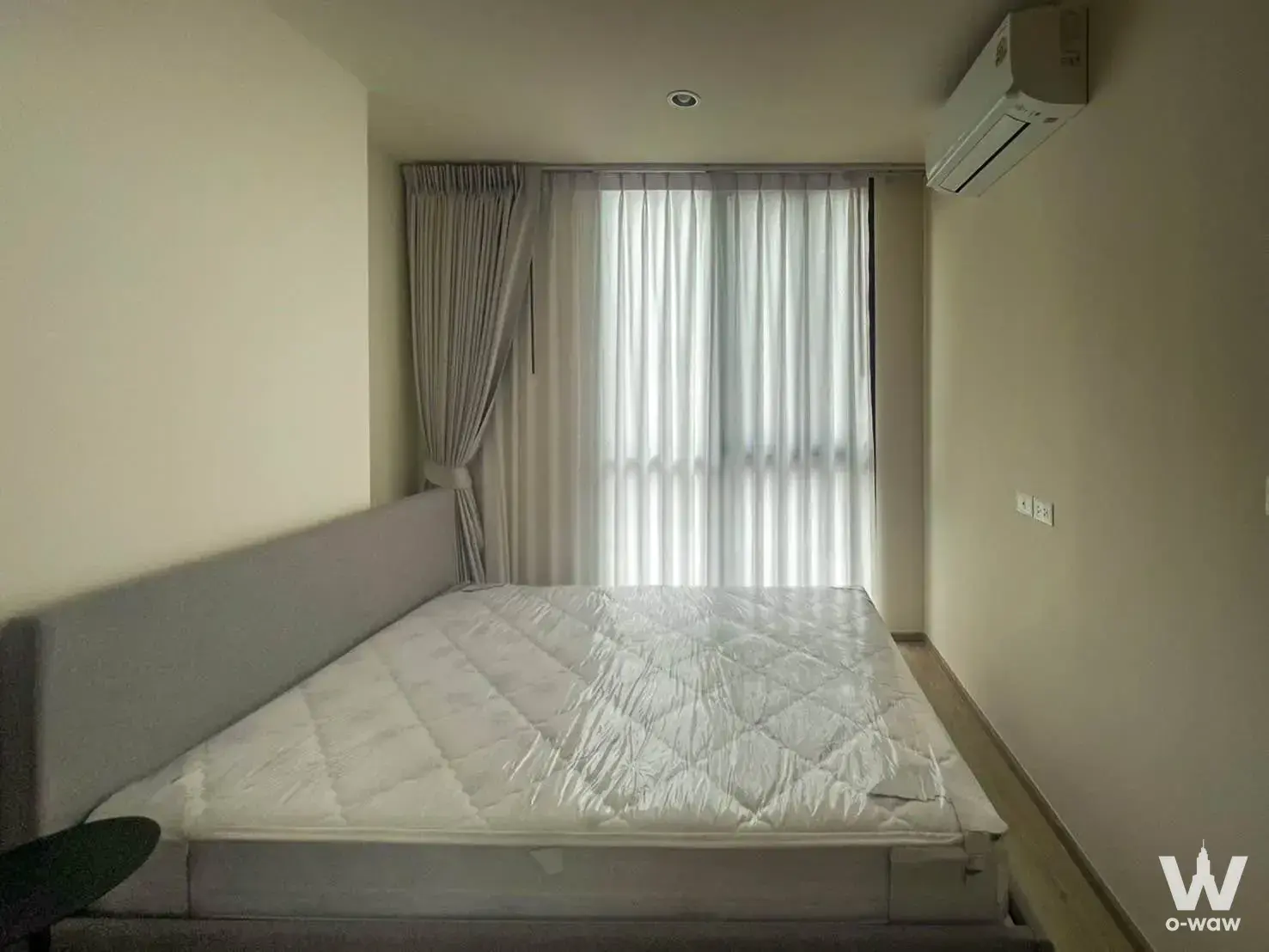Unmade queen bed with plastic wrap in a minimalist 1-bed bedroom at Nue District R9