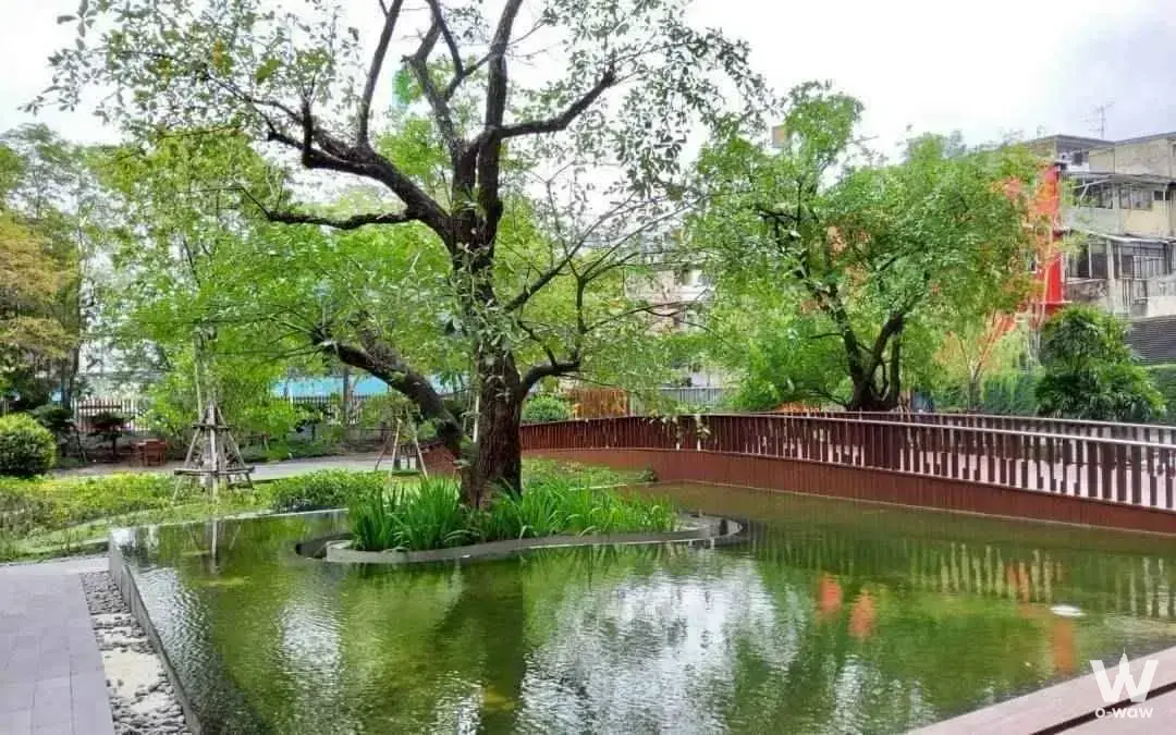 Landscaped garden pond with mature tree and curved metal walkway at Parco Condominium