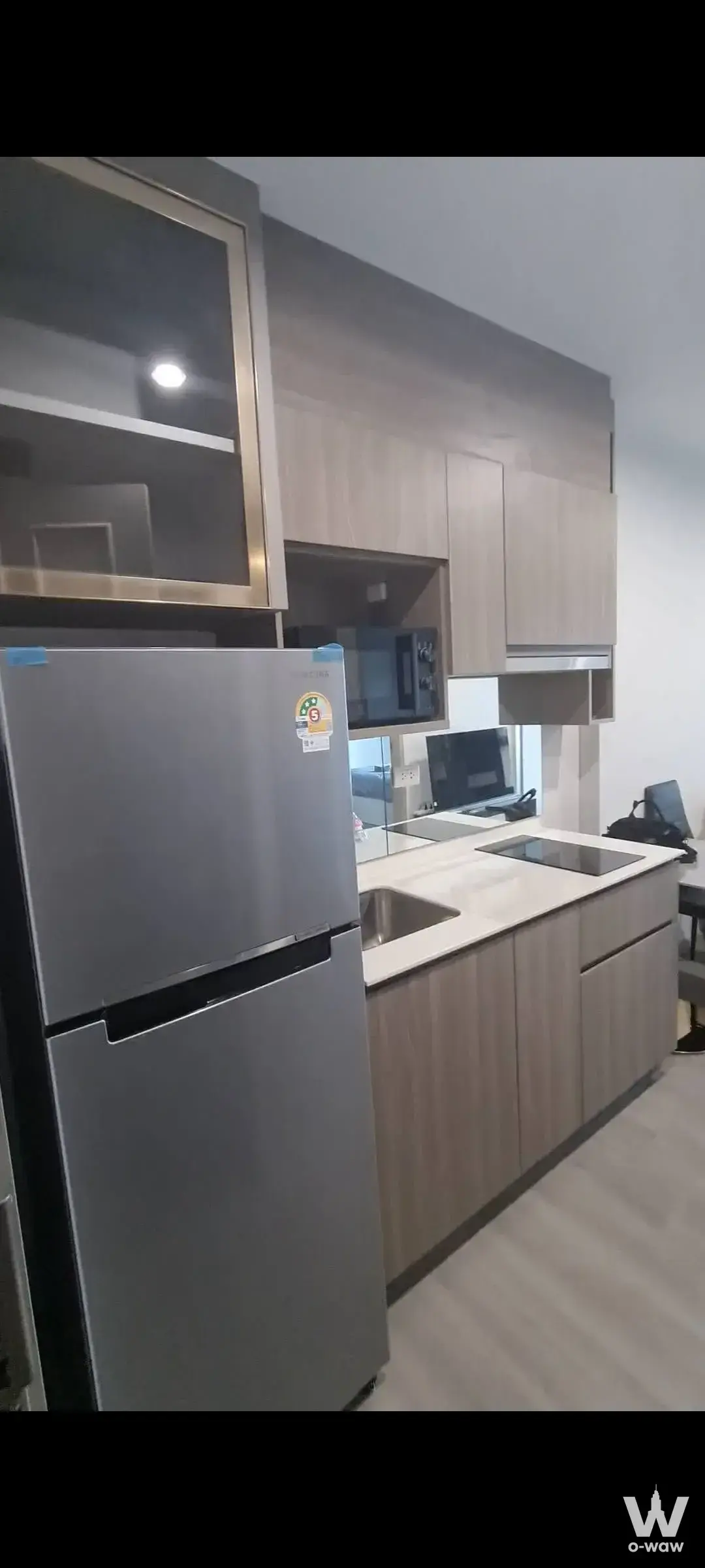 Fully furnished kitchen in The Parkland Bangna condo with oak cabinetry, glass display cabinet, and stainless steel