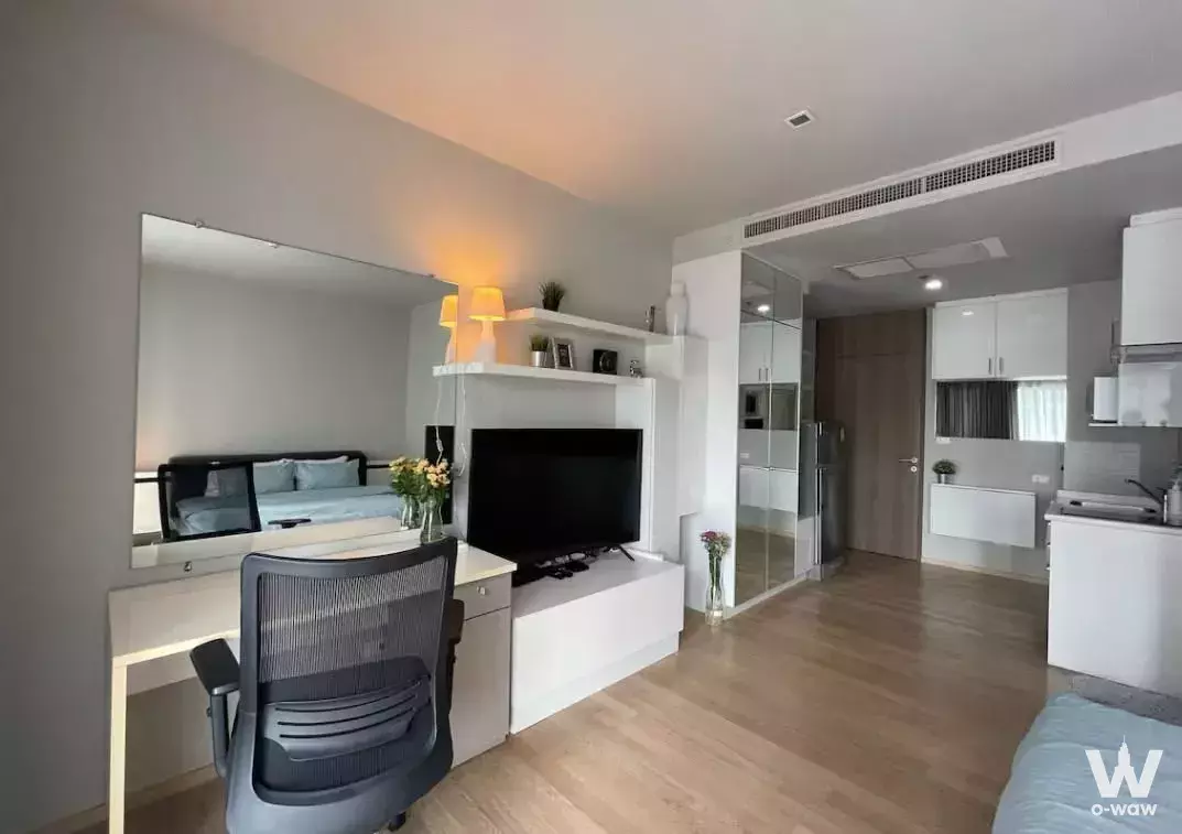 Open-plan studio in Noble Refine with a white desk, built-in TV unit, and light wood flooring