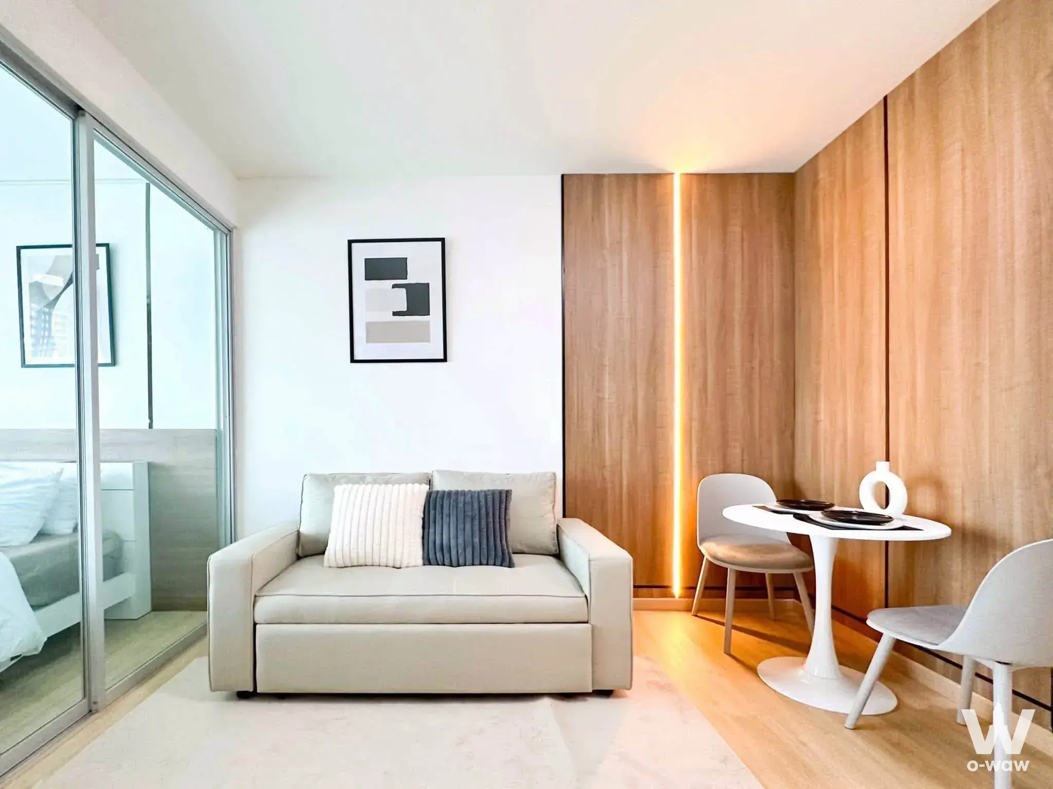 Studio living area in an A space Sukhumvit 77 condo for sale featuring beige sofa bed and wood accent wall