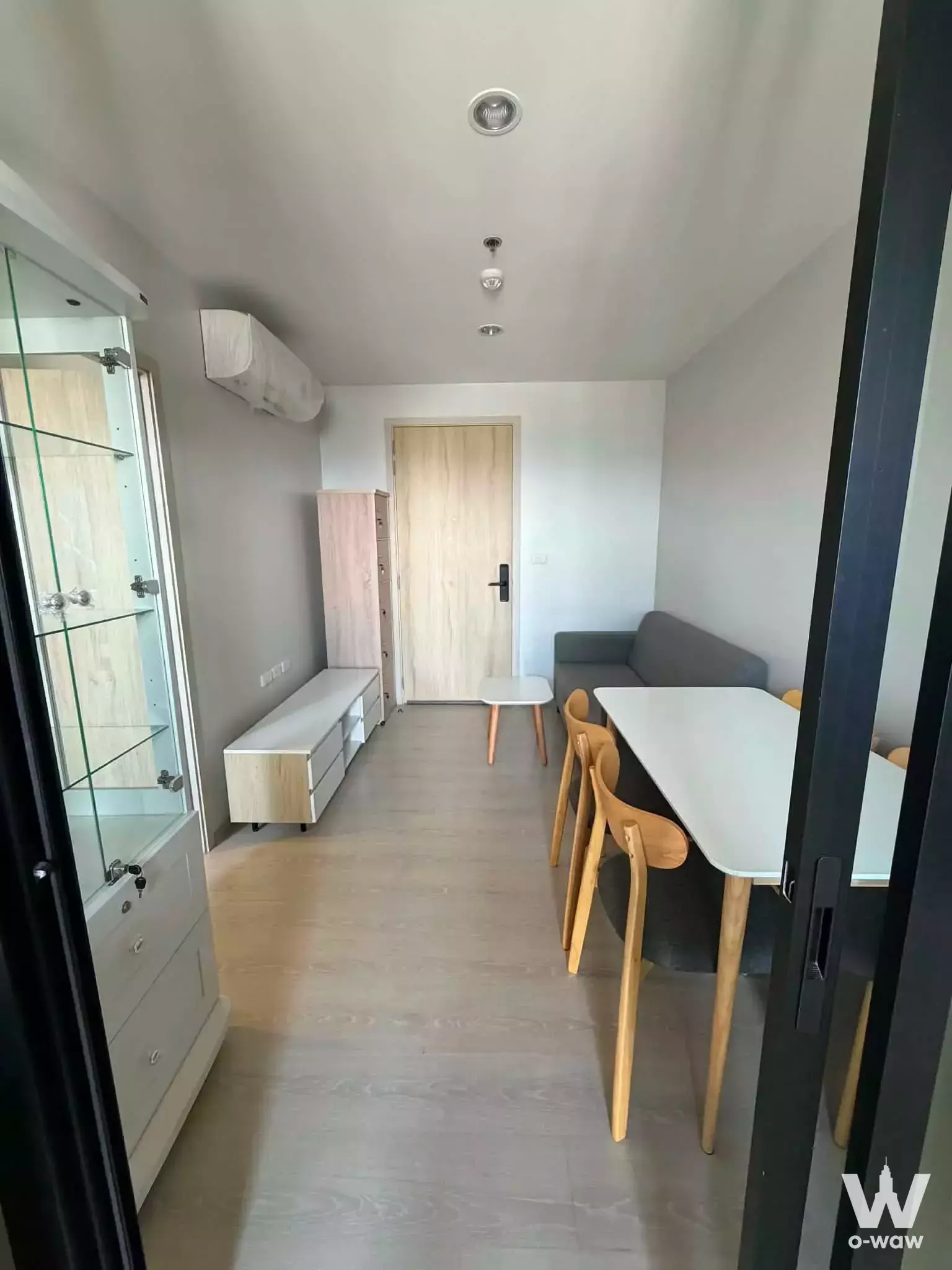 Studio living area in a NUE Noble Srinakarin Lasalle unit with a dining set, grey sofa, and light wood flooring