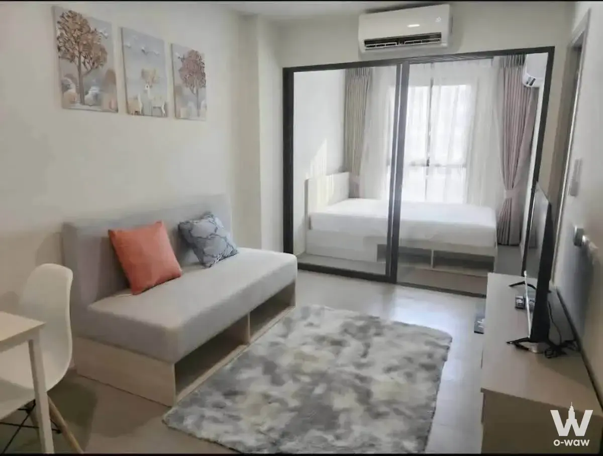Open-plan living area in a Sukhumvit 93 condo with grey sofa and black-framed glass partition