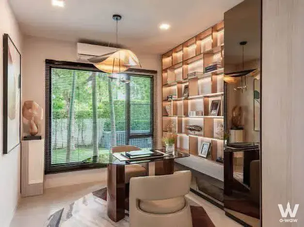 Home office in Mantana Bangna house featuring built-in bookshelf and lush window view