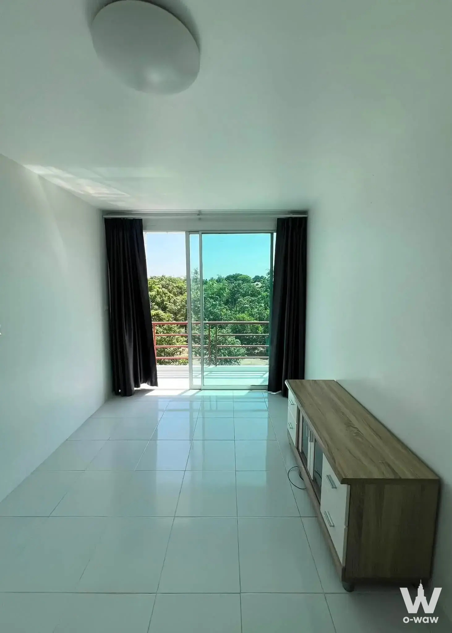 Empty living room in a Grand Bangkok Boulevard house with white tile floors and sliding doors opening to a green balcony