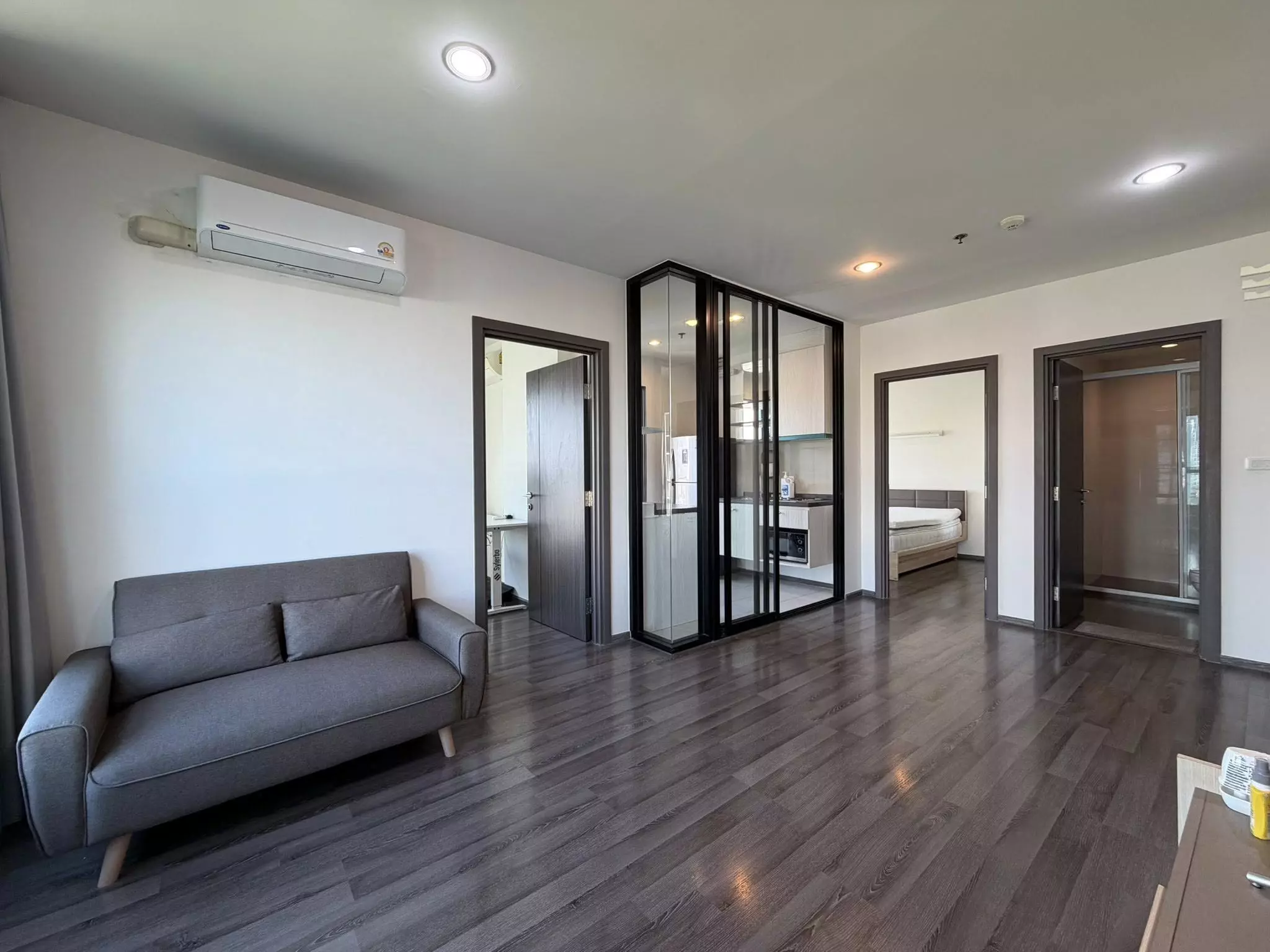 Living room in a 2-bed THE BASE Park West condo with grey sofa and glass kitchen partition