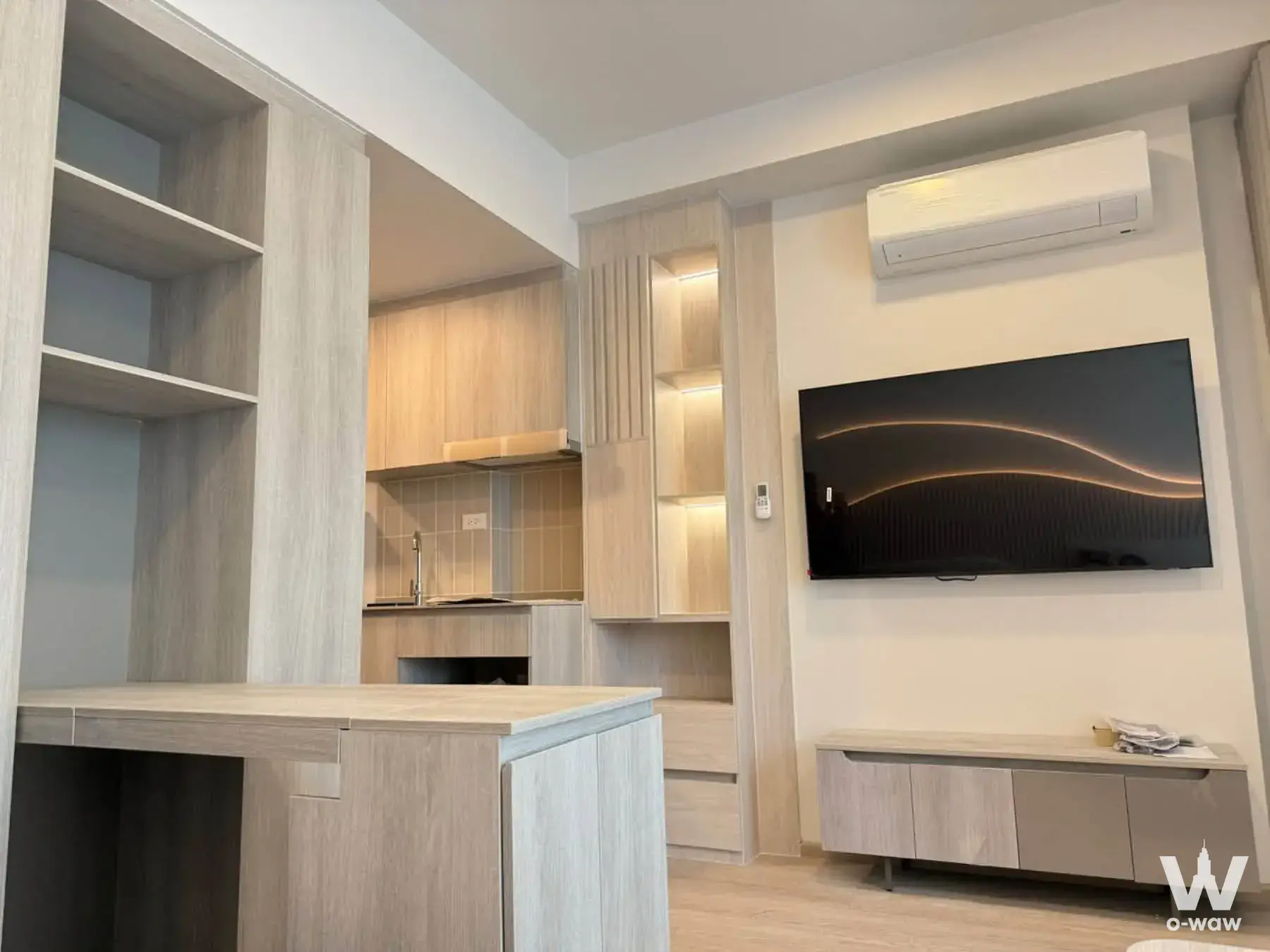 Open-plan living area in COBE Kaset-Sripatum featuring light oak floors and built-in cabinetry