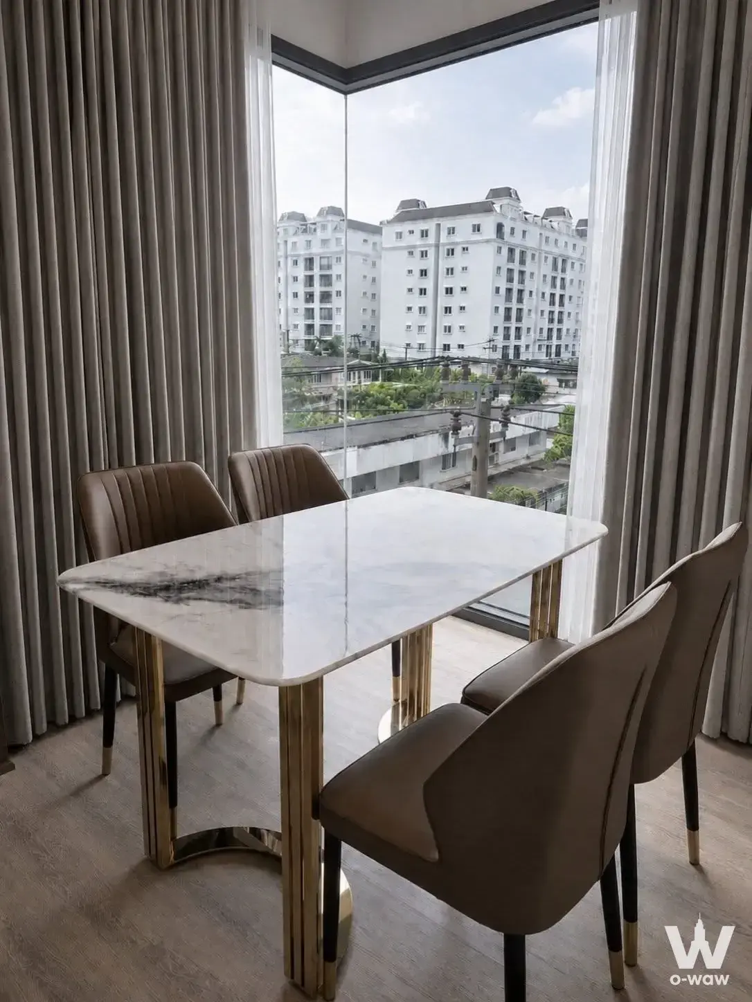 Dining area in PYNN Soonvijai with marble table and taupe chairs facing a corner window view