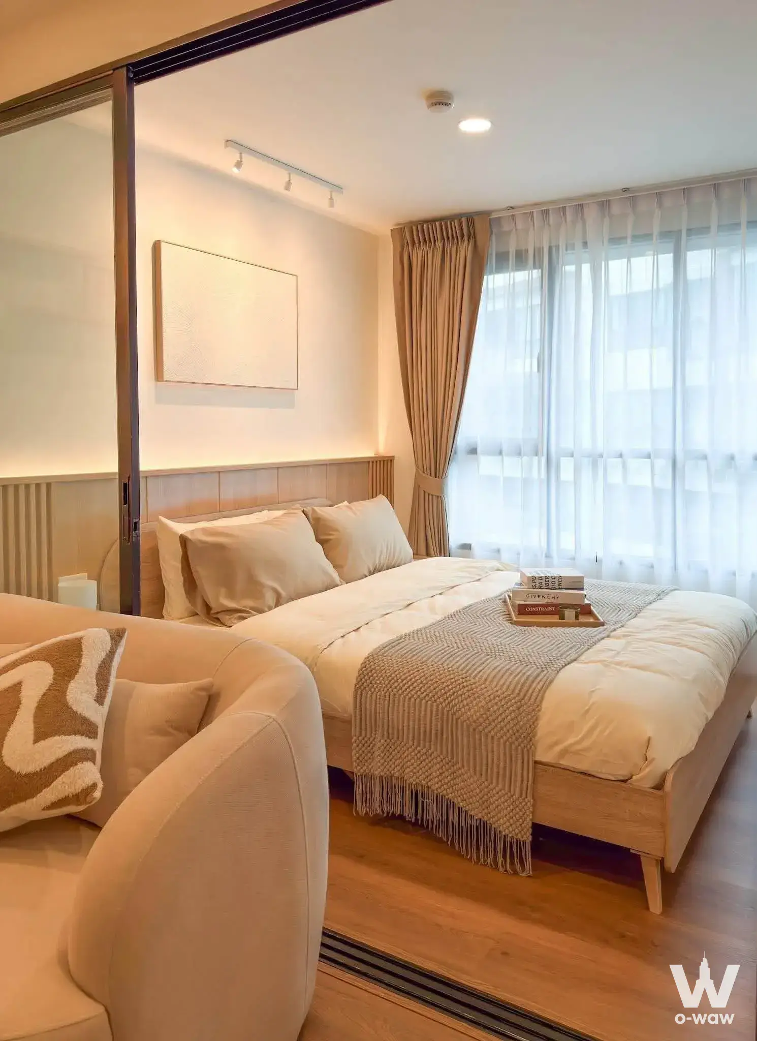 This minimalist bedroom has a light-wood bed, fluted headboard and floor-to-ceiling window in a Centrio Phuket condo for sale