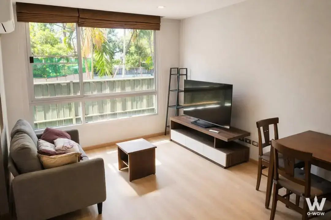 Living room with grey sofa, dark wood furniture, and bamboo blinds in a Sukhumvit 42 condo