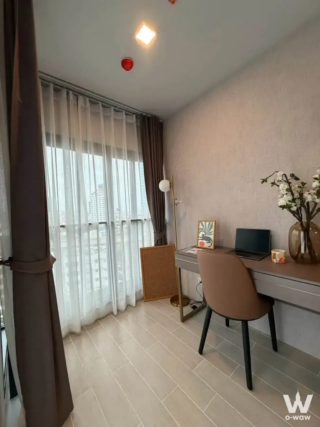 The home office nook in a Life Phahon-Ladprao 1-bed rental has a floating desk and city skyline view