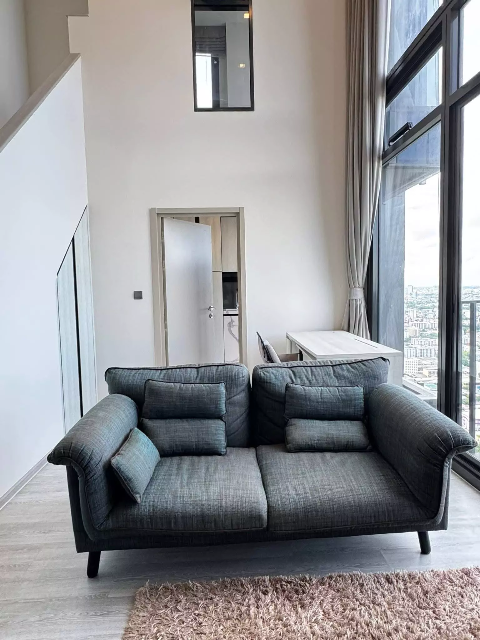 Loft-style living room with grey sofa and floor-to-ceiling windows in a 1-bed condo for rent at THE LINE Sukhumvit 71