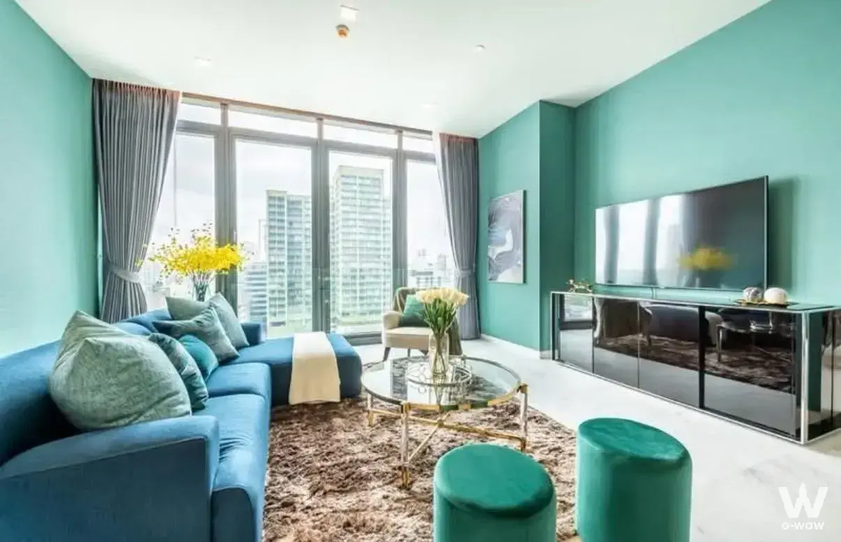2-bed condo for sale in The Monument Thong Lo living room with teal walls, blue velvet sectional sofa, and city skyline view