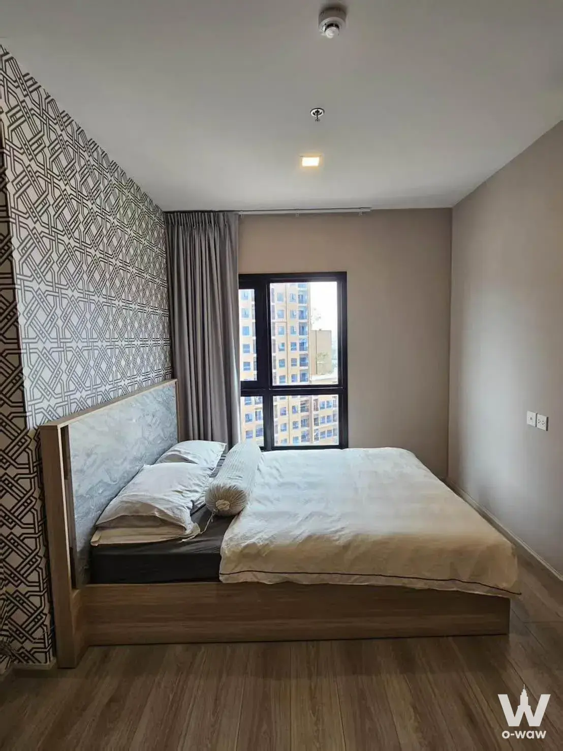 Queen bed in an M Ladprao condo featuring geometric wallpaper accent wall and sliding glass door