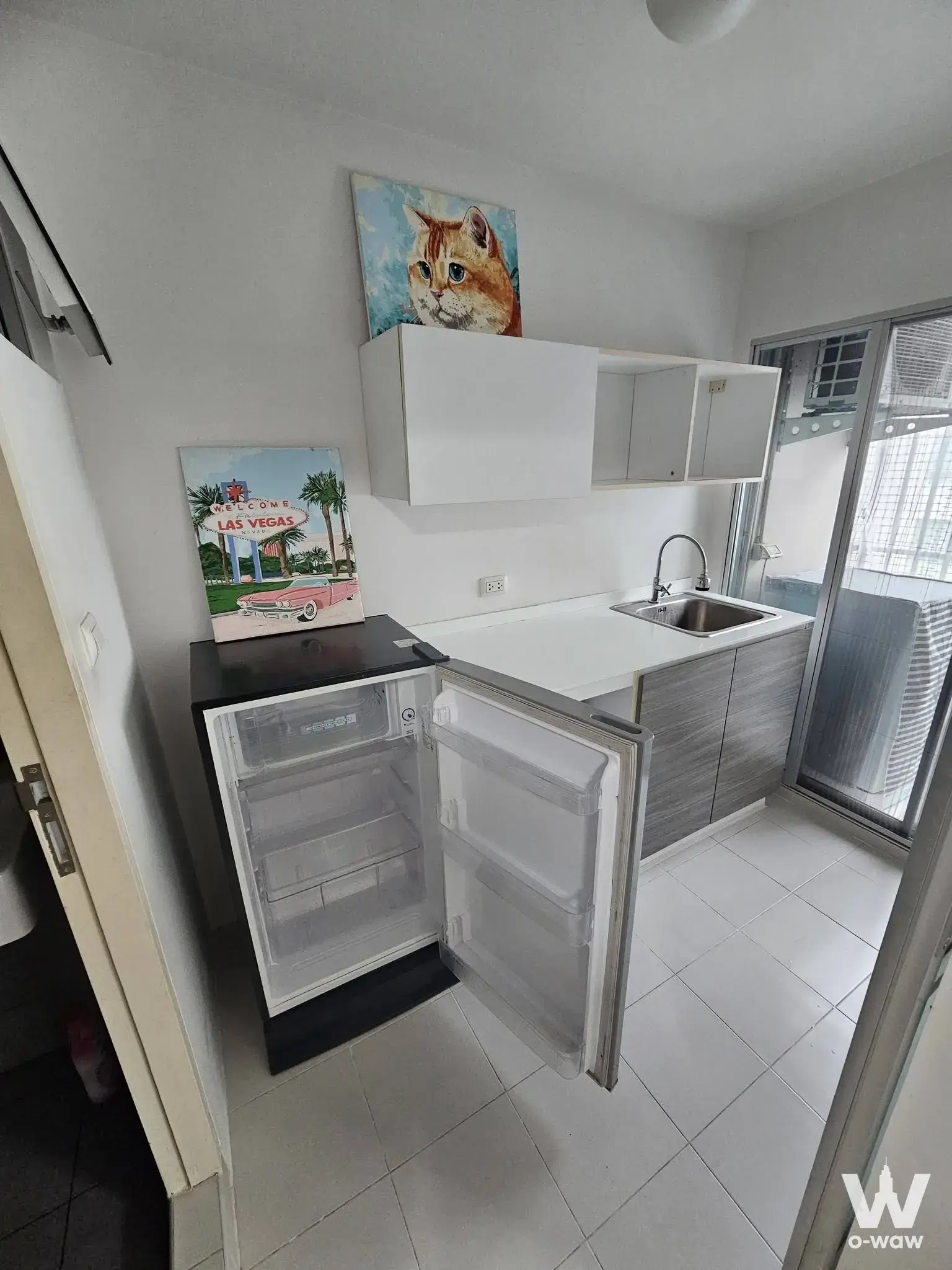 Compact kitchenette in dcondo Campus Resort Bangna with grey cabinets and a sliding glass door to the balcony