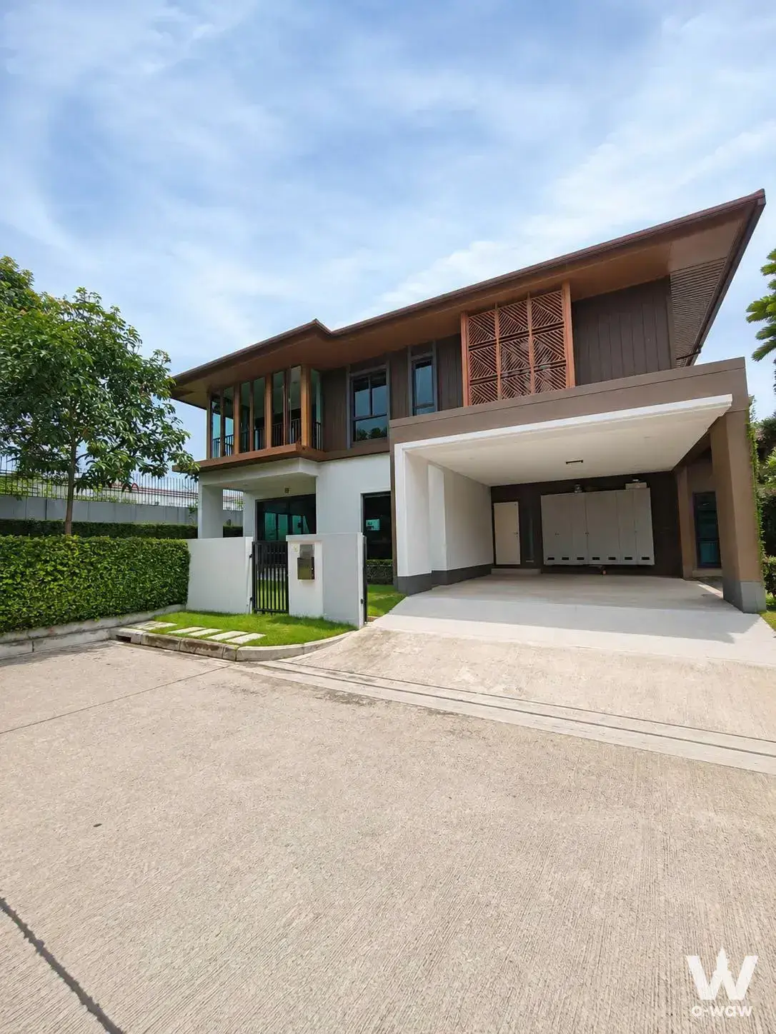 Two-story modern detached house with brown wood cladding, white stucco, and green lawn for sale at Burasiri Pattanakarn