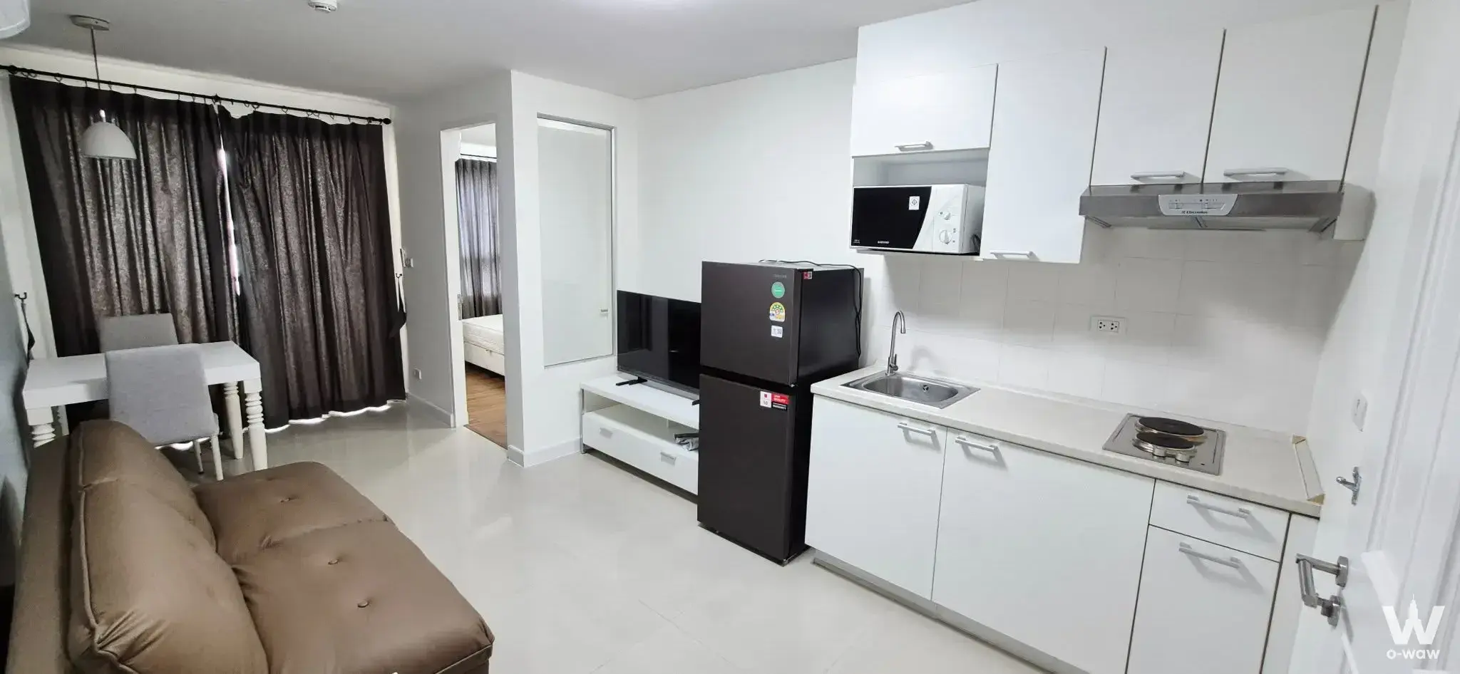 1-bed condo for rent in The Clover Thonglor Residence with open-plan living, brown leather sofa, and modern kitchenette