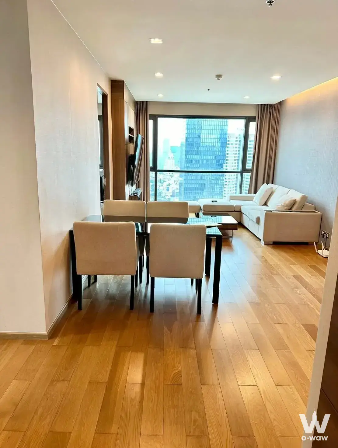 Open-plan living area with oak flooring and high-floor city skyline view at The Address Sathon