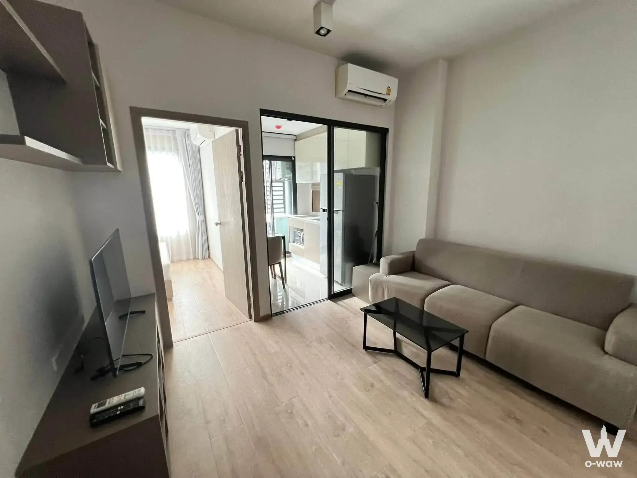 Furnished living room in IDEO Rama 9 Asoke condo with taupe sofa, wood-look flooring, and neutral palette