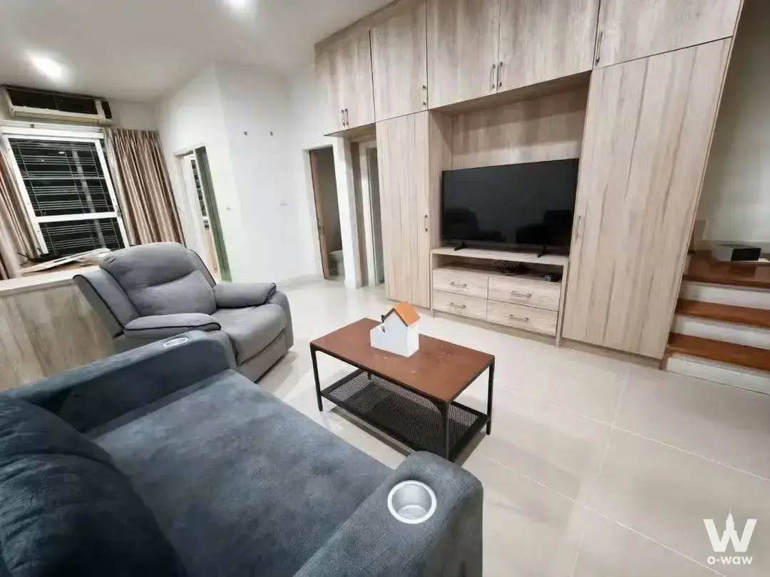 This living room in a 3-bed townhouse for rent in S-Sense Sathorn-Taksin has a grey sofa and TV wall unit