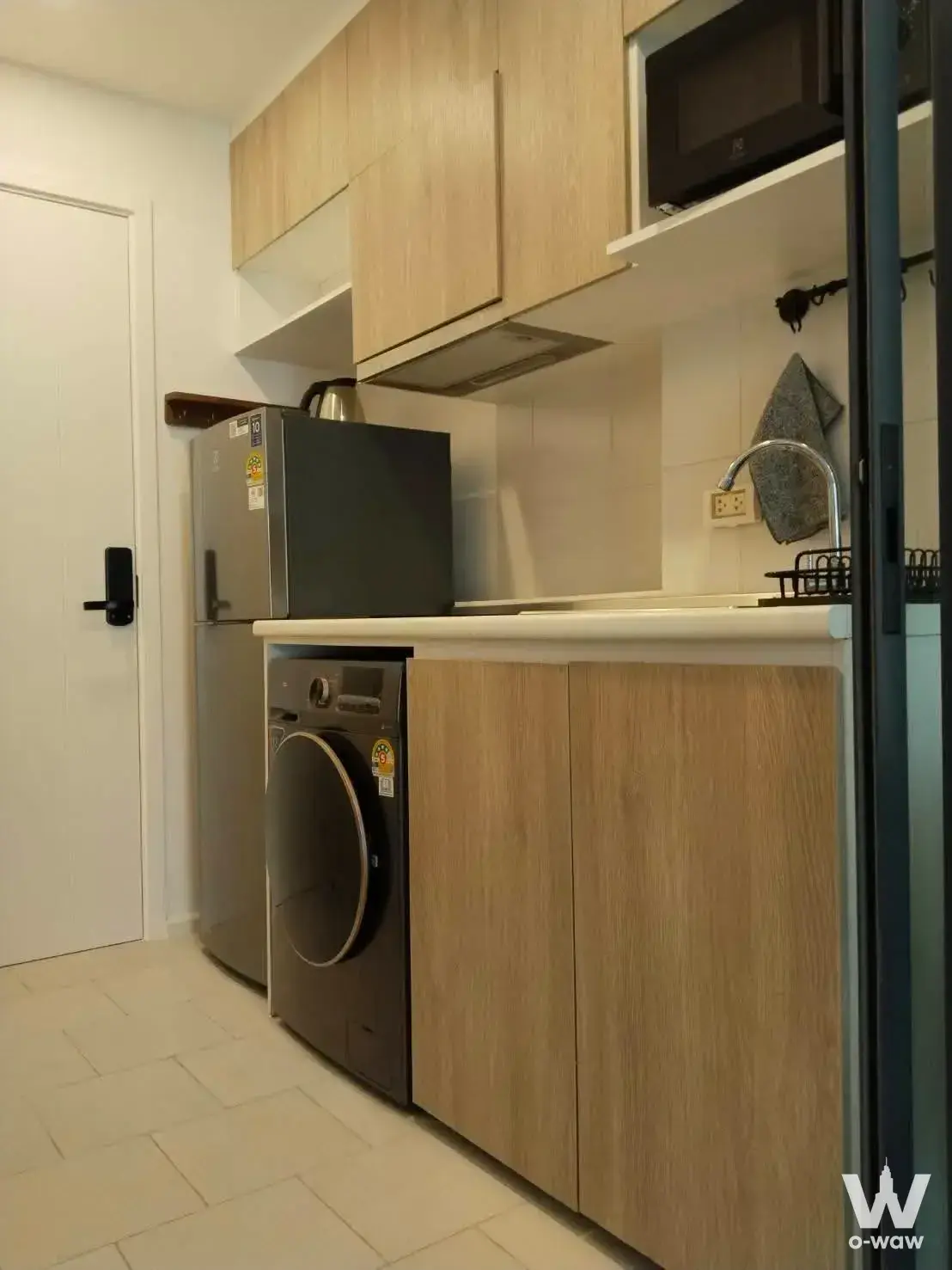 Compact kitchenette in a DENIM Jatujak rental with light wood cabinets, stainless fridge, and built-in washing machine