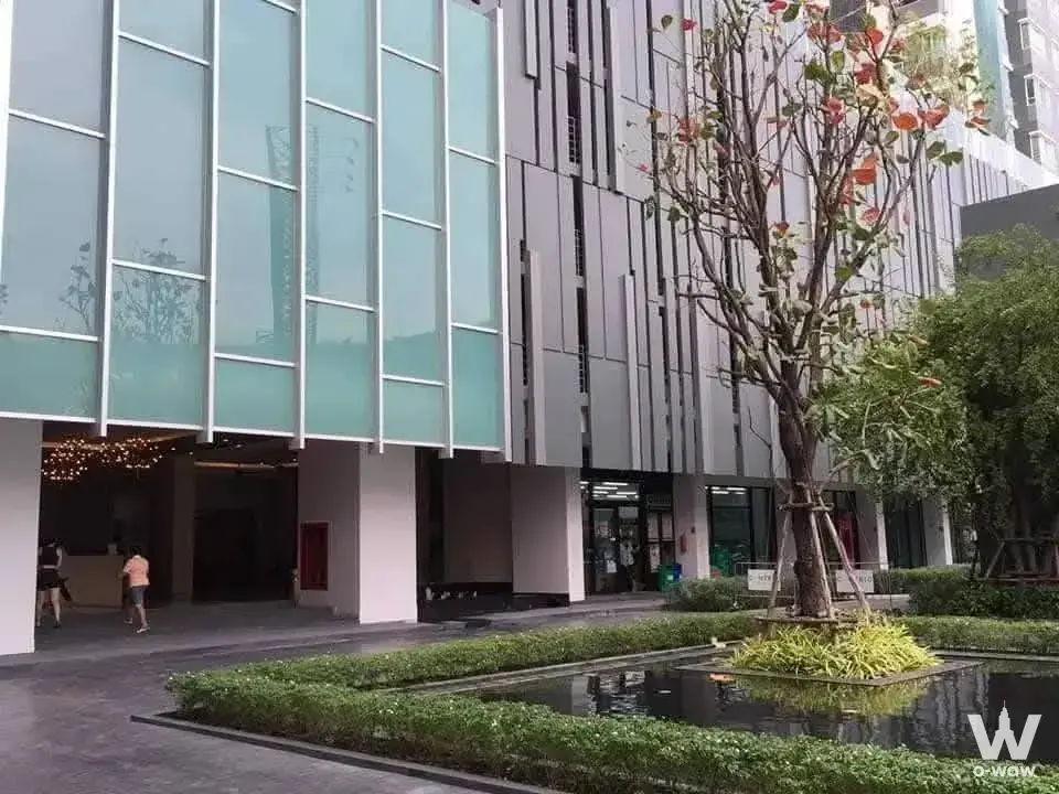 Centric Tiwanon Station condo exterior with glass lobby, water feature, and lush landscaping