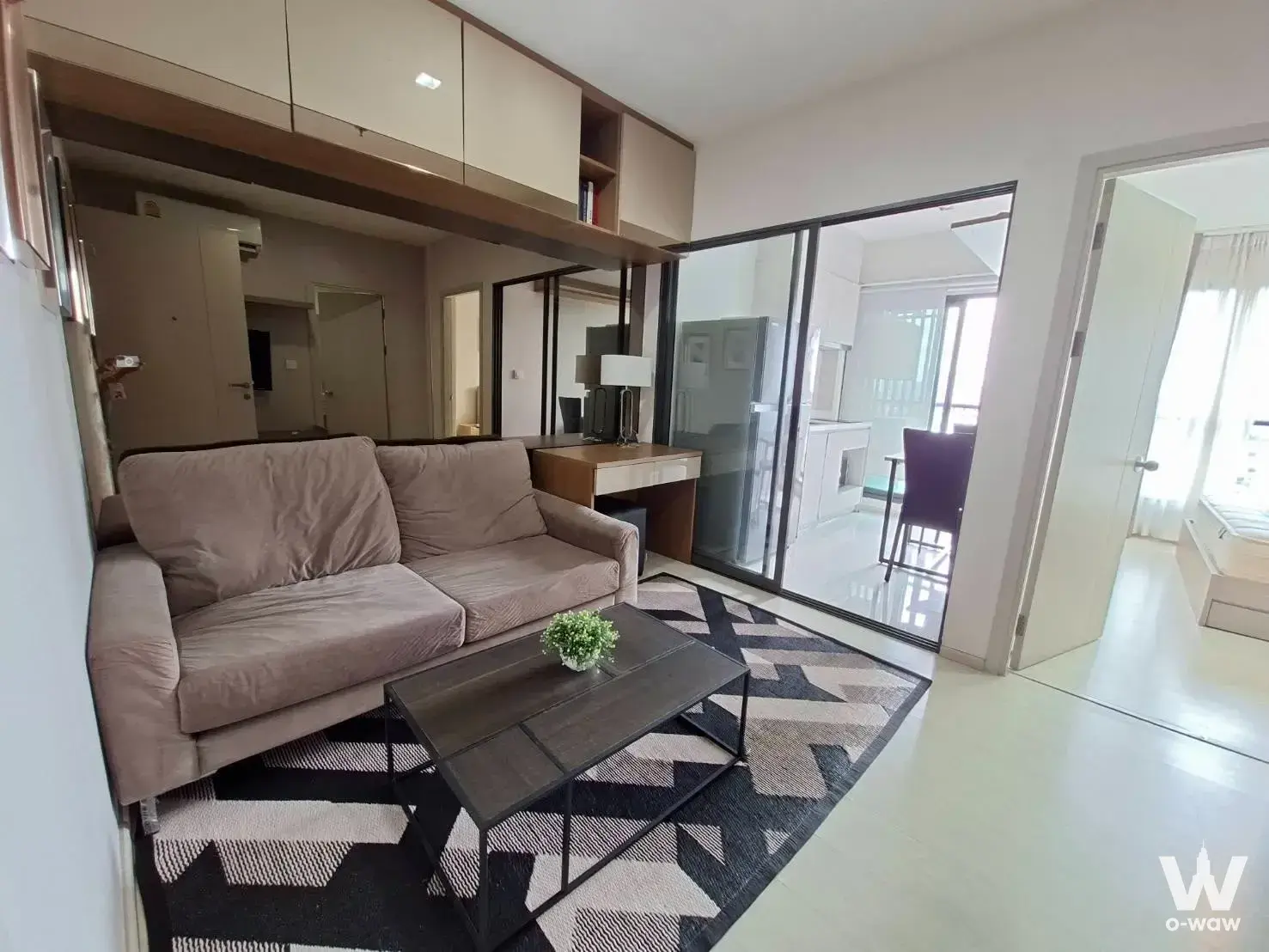 Furnished living room in a Life Sukhumvit 48 one-bedroom rental with taupe sofa, glass partition and bedroom view
