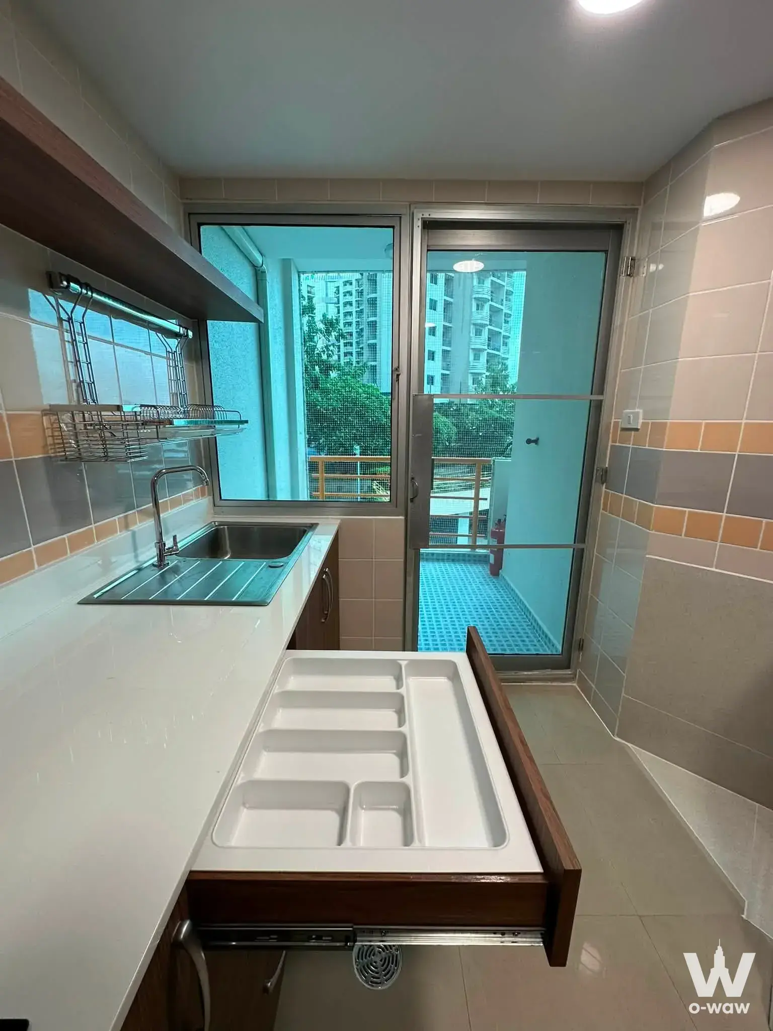 Narrow kitchen utility area in SV City Rama 3 condo with stainless steel sink, colorful tiled backsplash, and service balcony