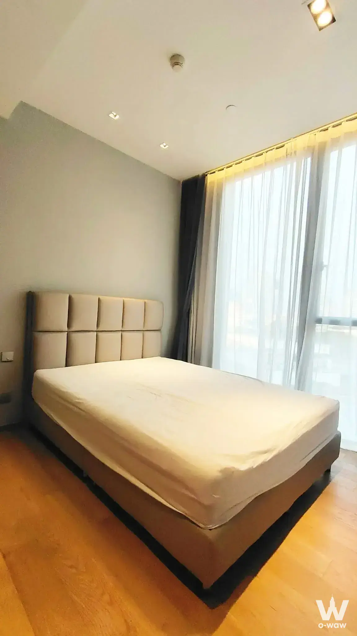 A queen bed with beige headboard and layered curtains is in a BEATNIQ 2-bed condo bedroom with sage walls