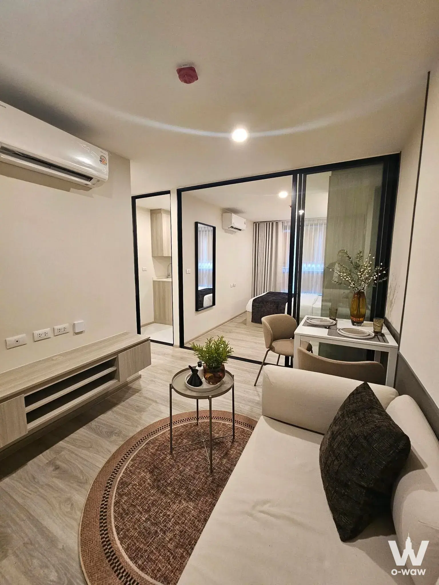 Staged living room in Origin Play Sri Udom Station condo with light wood flooring and glass partition