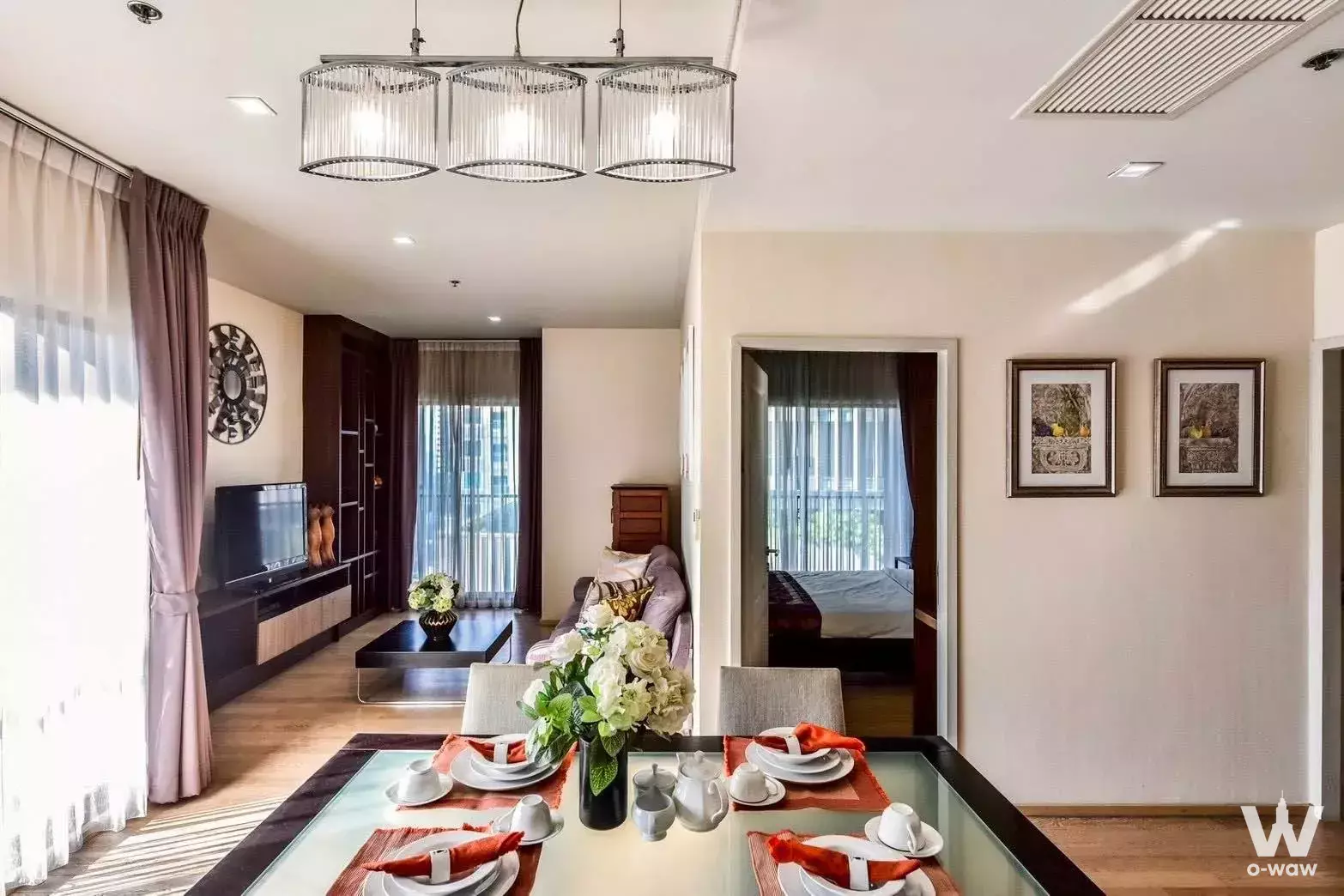 Dining and living area in a 2-bed Noble Refine condo with crystal chandelier and orange accents
