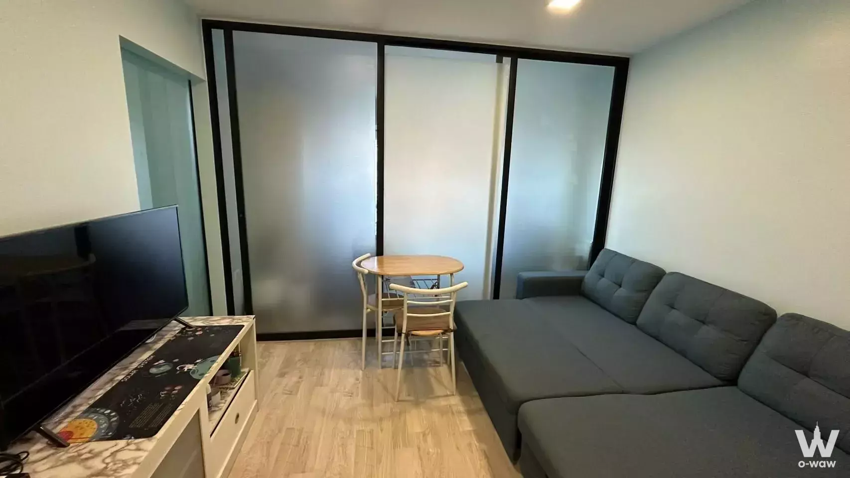 Grey sectional sofa and frosted glass partition in a compact living room at The 1 Plus Grand Ramkhamhaeng
