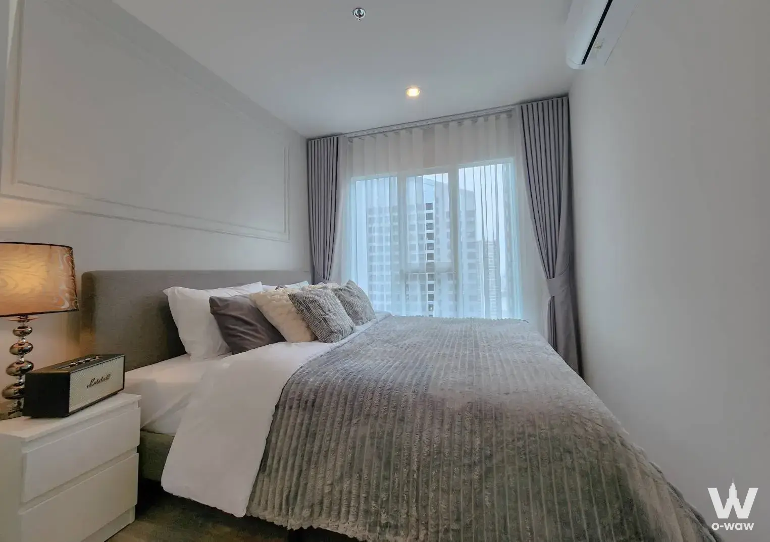 Queen bed room in Regent Home Bangna condo with grey drapes and high-rise city view