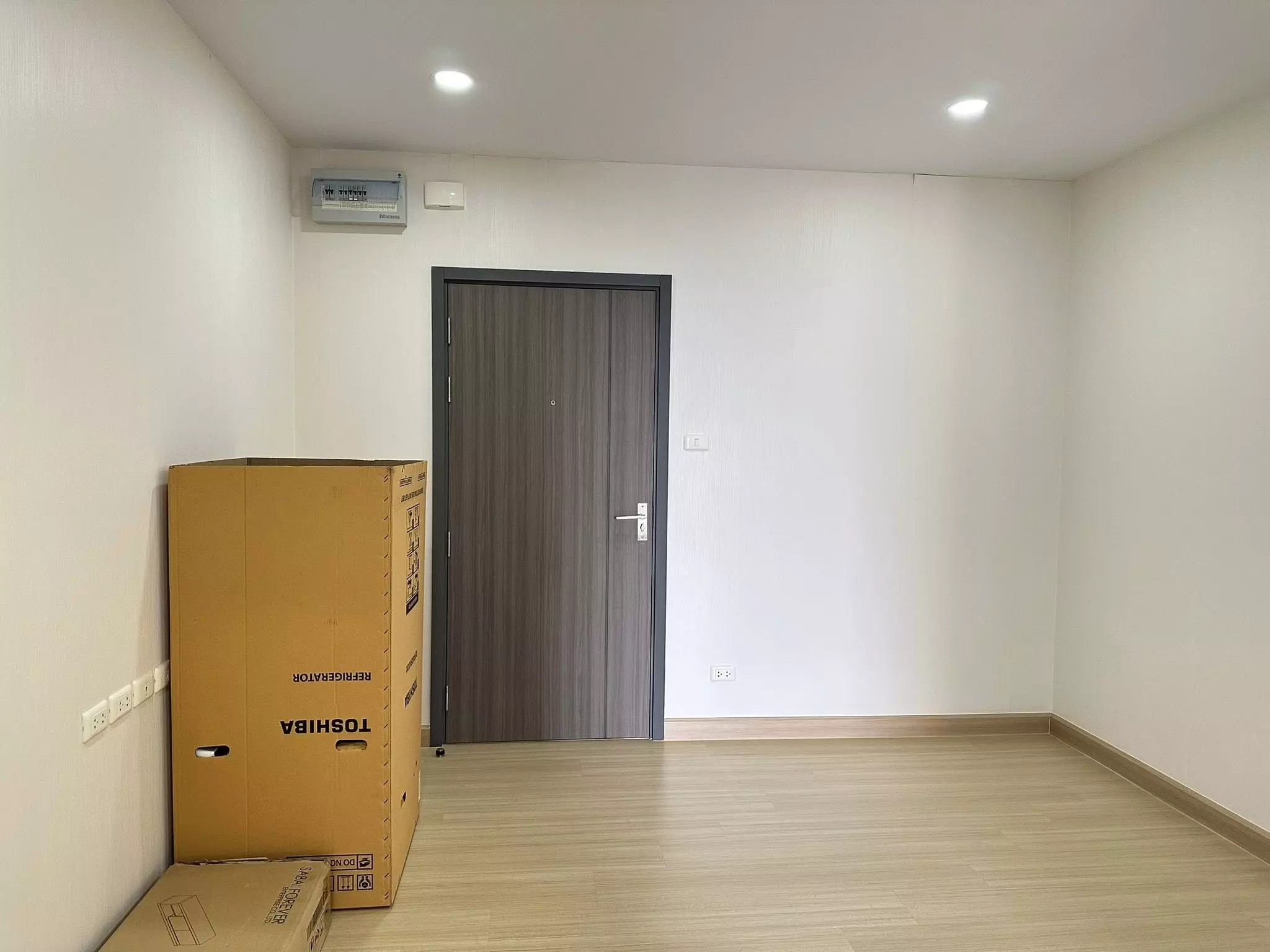 Empty room with light wood flooring and moving boxes in a 1-bed condo for sale at Supalai Veranda Phasi Charoen