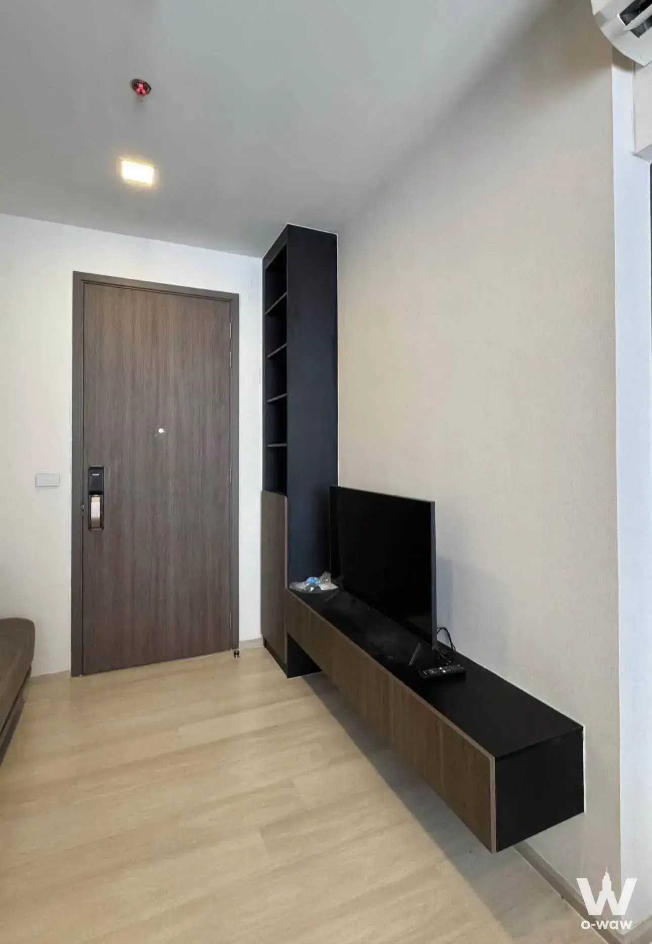 Living room entryway of a 1-bed condo for rent in The Privacy Jatujak featuring light wood flooring and black open shelving