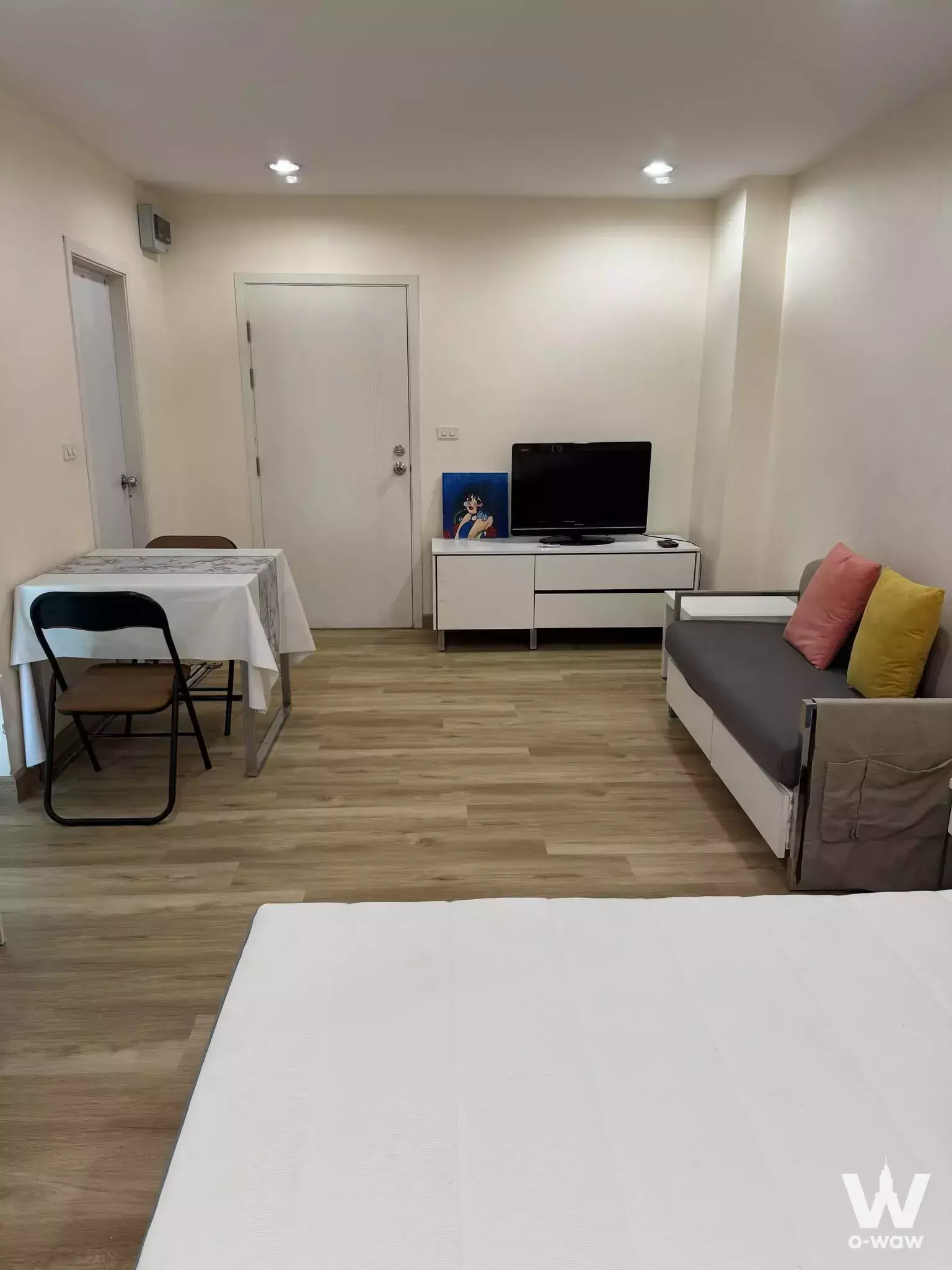 Furnished Premio Fresco studio showing grey sofa bed, white mattress, and compact dining set