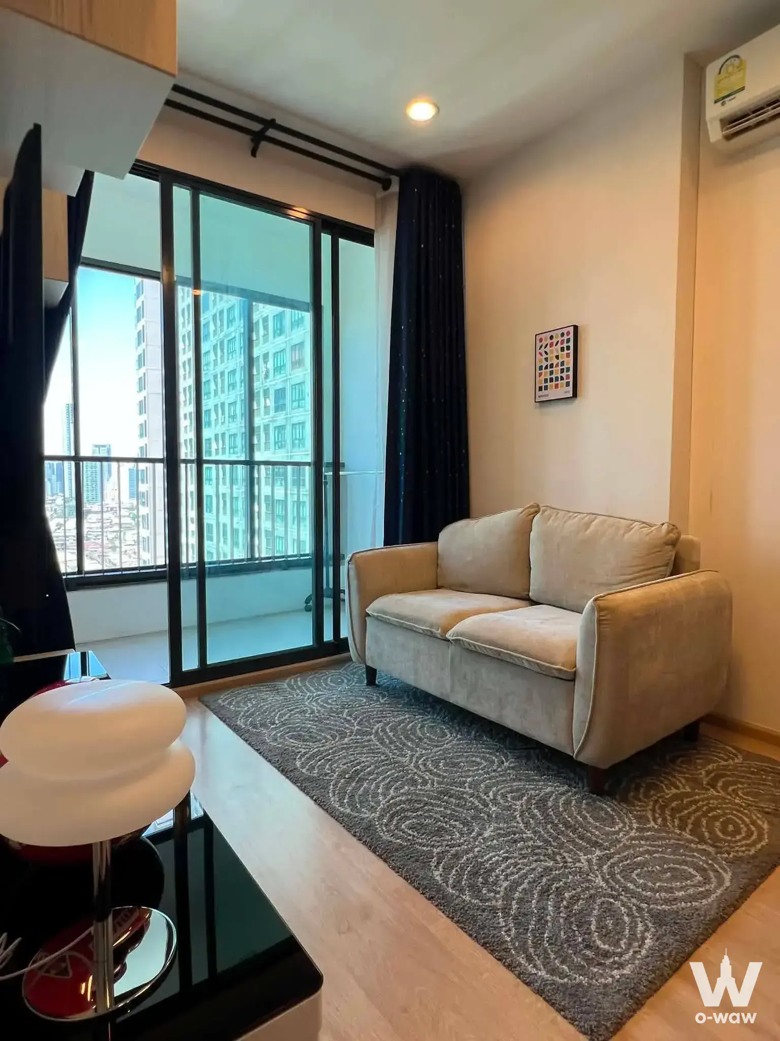 Ideo Sathon-Tha Phra 1-bed condo living room with beige sofa, grey rug, and high-floor city view