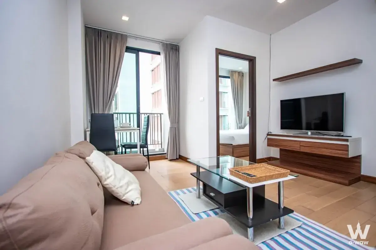 Modern living room featuring a tan sofa, glass coffee table, and balcony access in Astra Suites condo