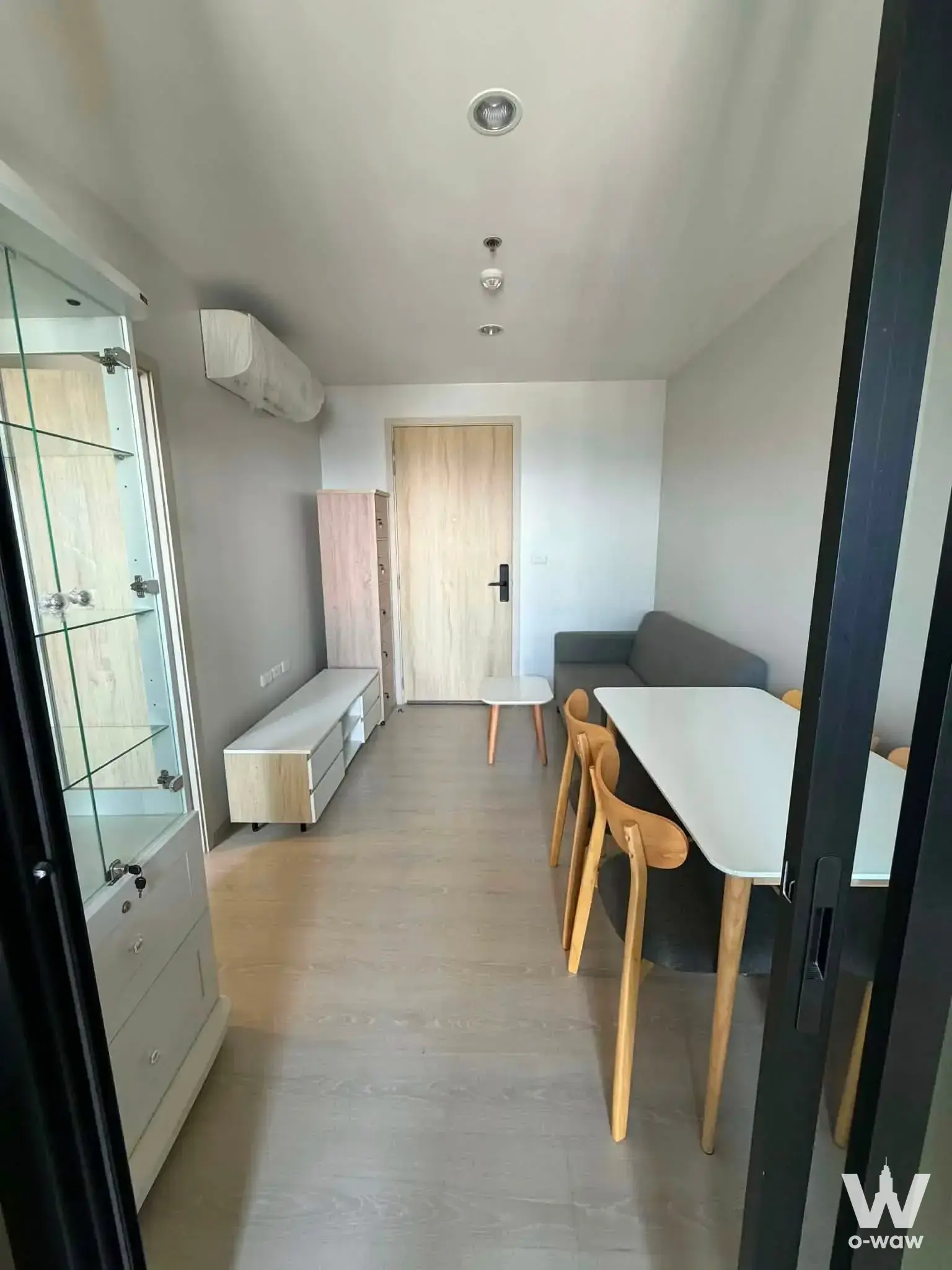 Noble Srinakarin Lasalle 1-bed for sale with minimalist living area, light wood floors, and grey sofa