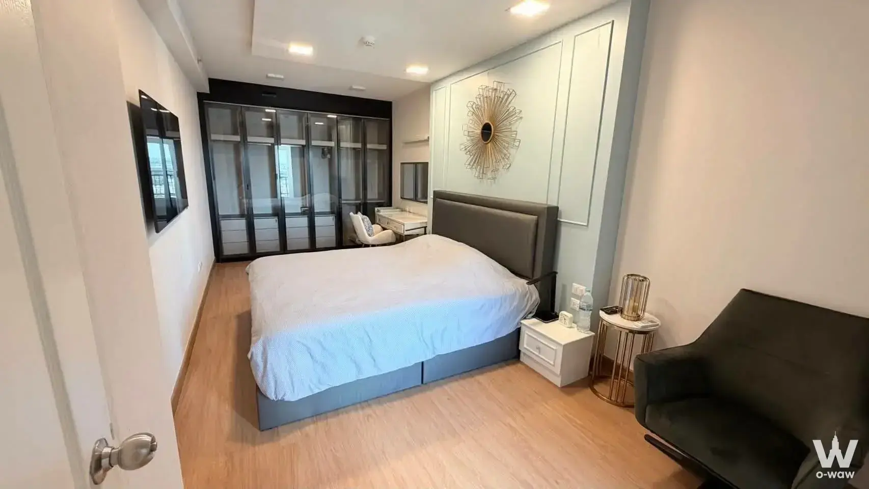 Bedroom in a Supalai Park Ekkamai unit with a grey king bed, gold sunburst mirror, and built-in wardrobe
