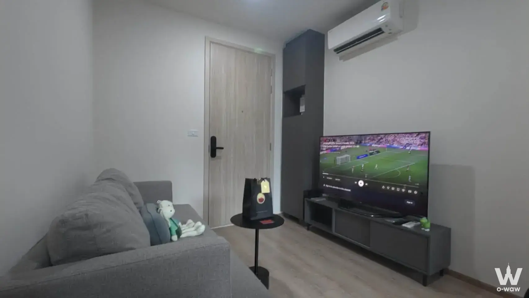 Living room in a Nue District R9 1-bed rental with a grey sofa, large TV and light wood flooring