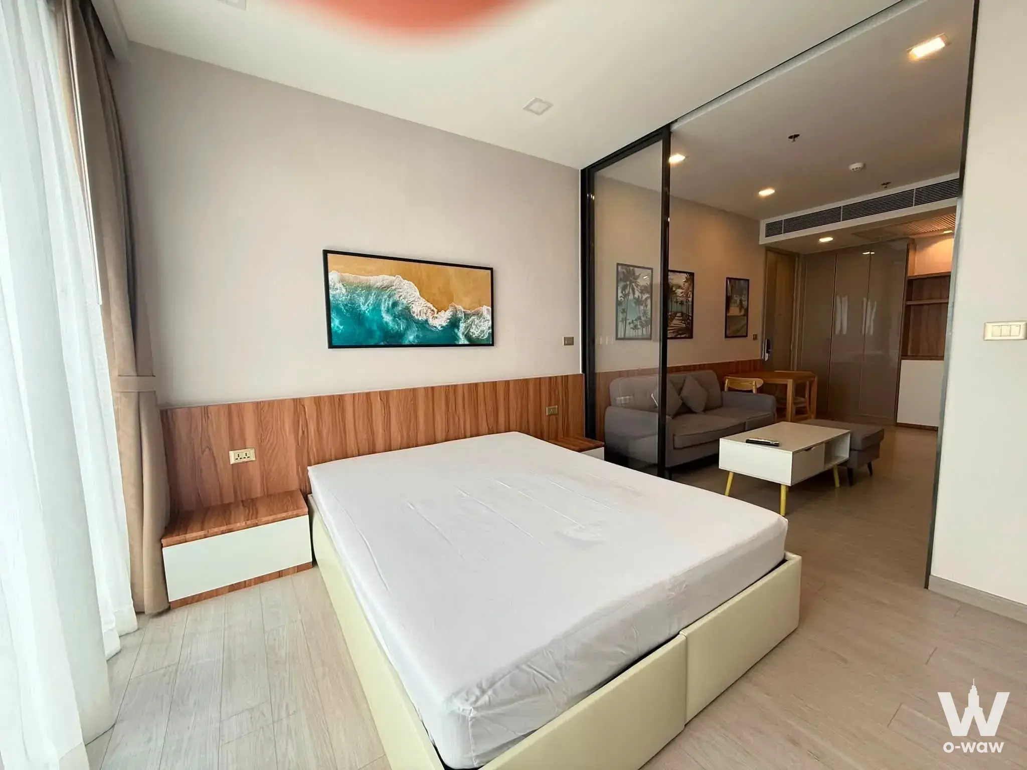 1-bed condo for rent in One9Five Asoke - Rama 9 bedroom with oak headboard wall, ocean artwork, and glass partition view