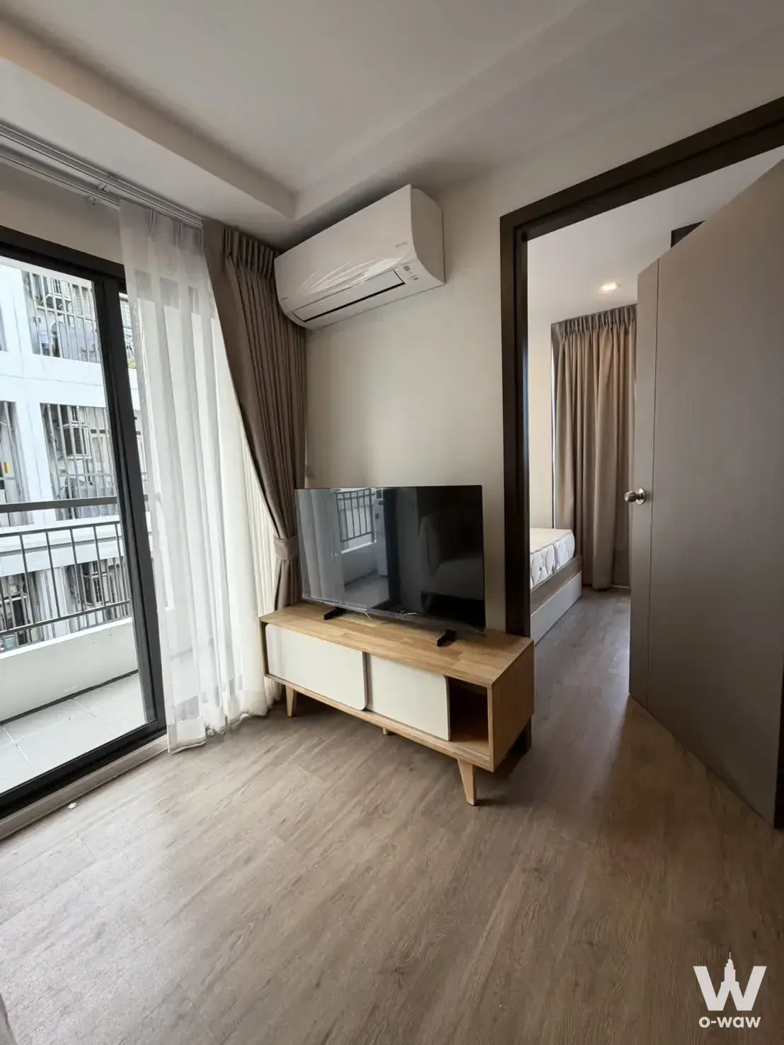 Furnished studio living area in The Nest Sukhumvit 64 with light wood floors and a large sliding glass door to the balcony